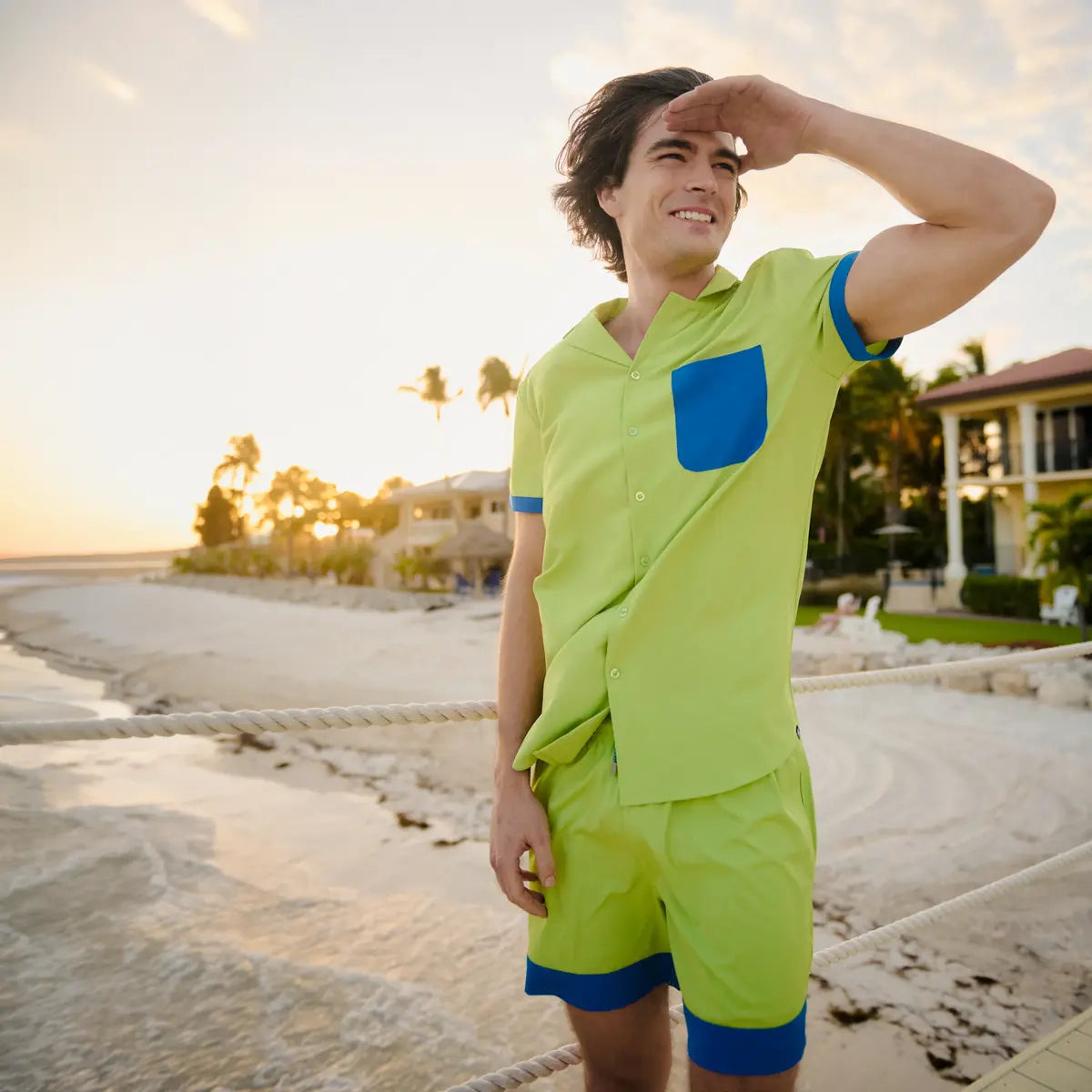 Person wearing a bright green shirt and shorts with blue accents on a beach.