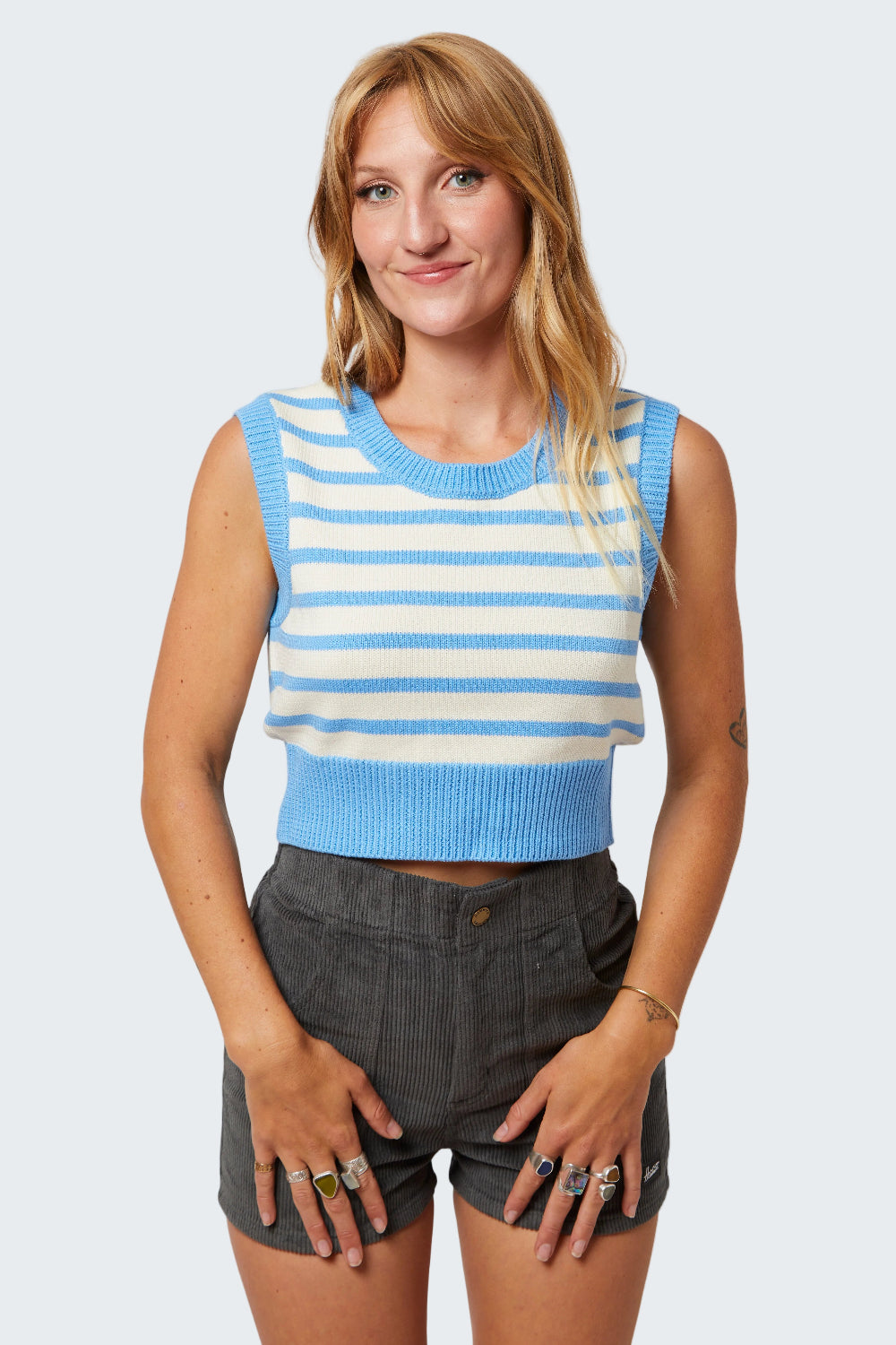 Woman wearing a blue and white striped sleeveless top with gray shorts on a white background