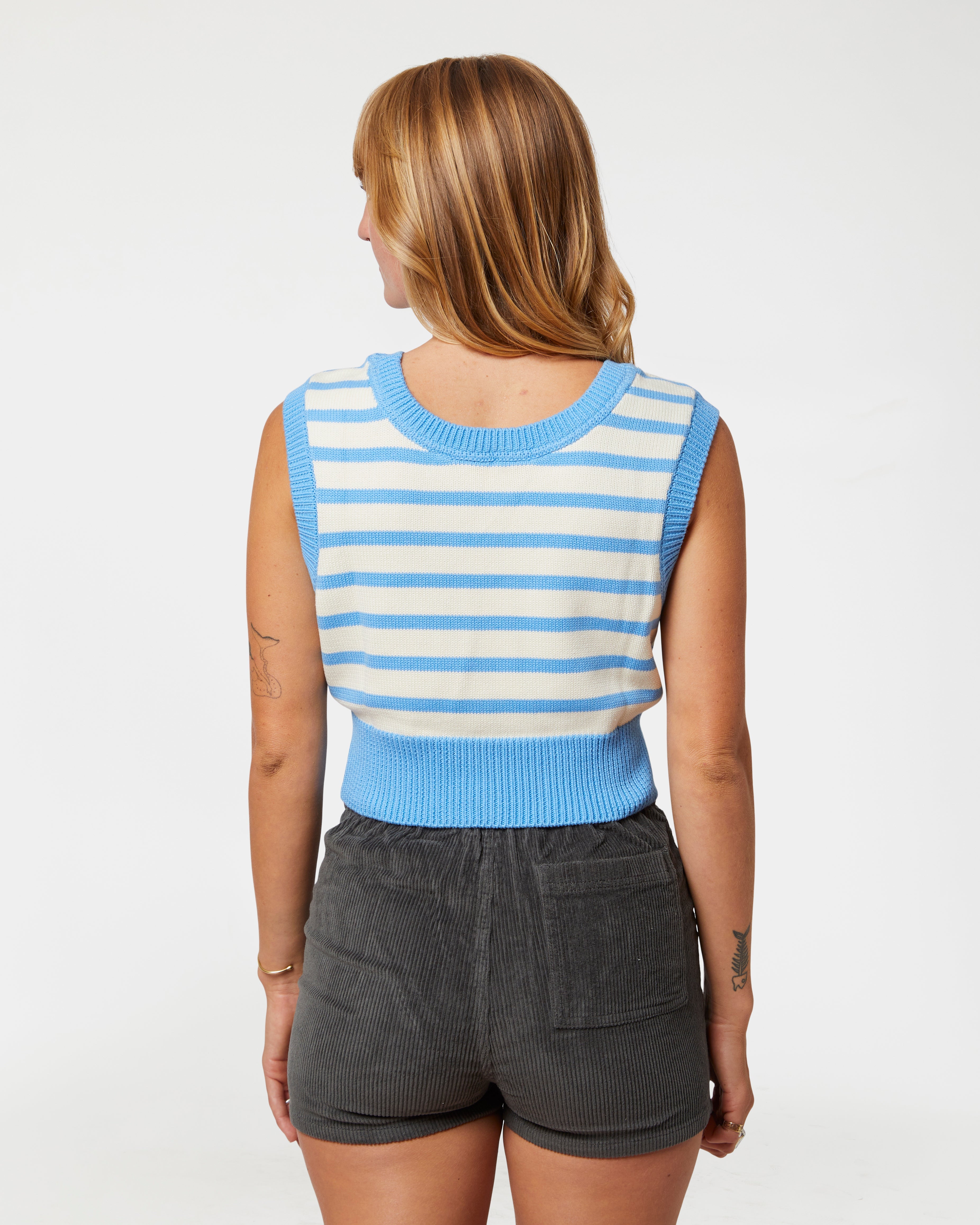 Woman wearing a blue and white striped sleeveless top and gray shorts on a white background