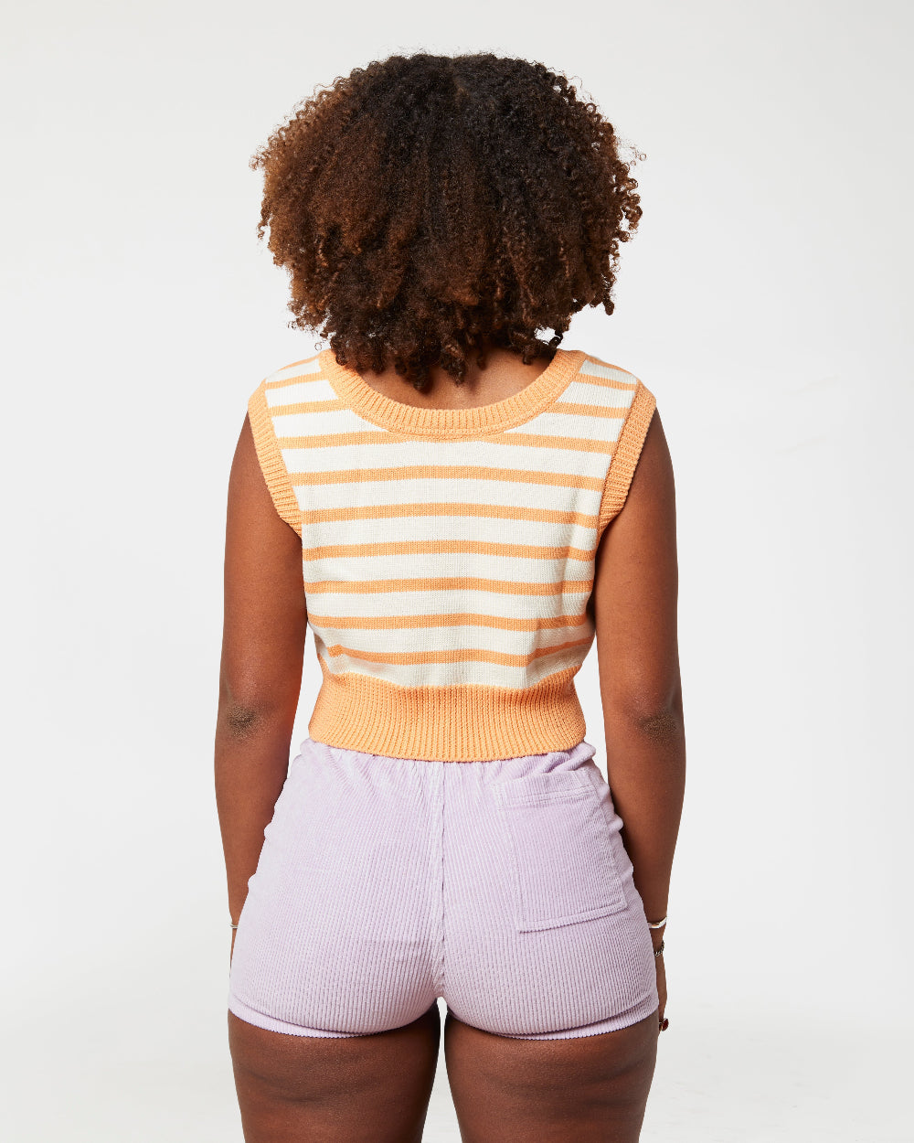 Person wearing a striped sleeveless top and light purple shorts on a white background