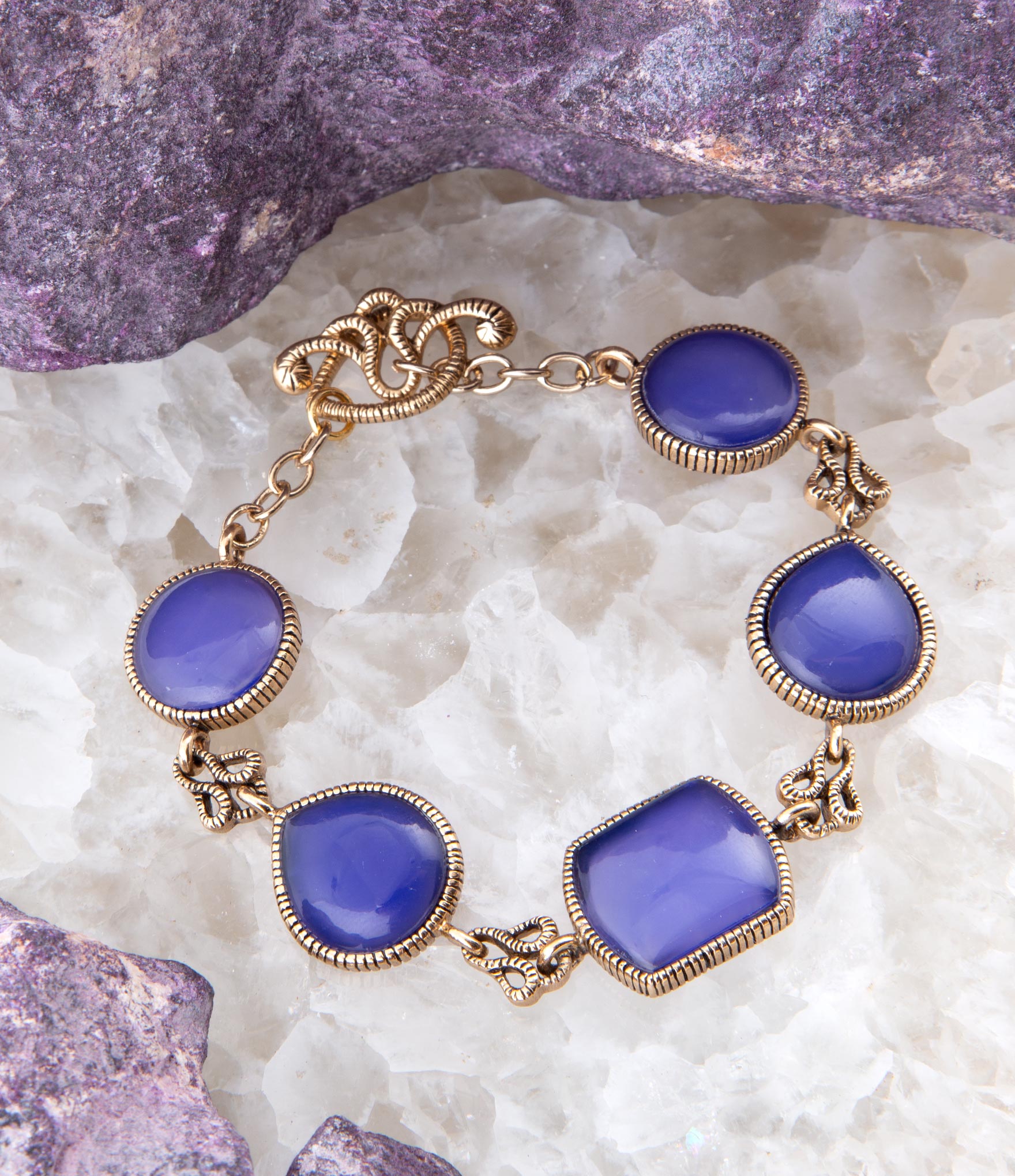 Bracelet with purple stones and gold accents on a textured white surface with purple stones.