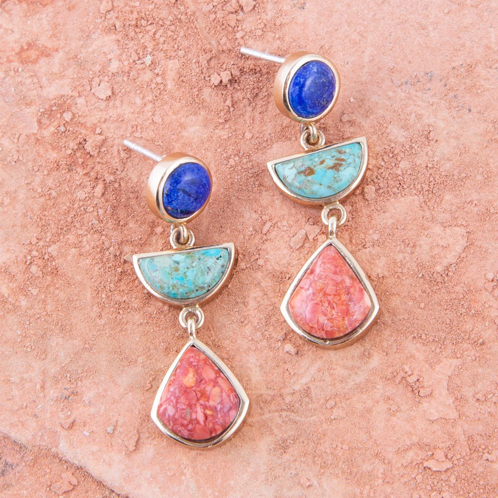 Colorful earrings with blue, turquoise, and pink stones on a textured pink surface