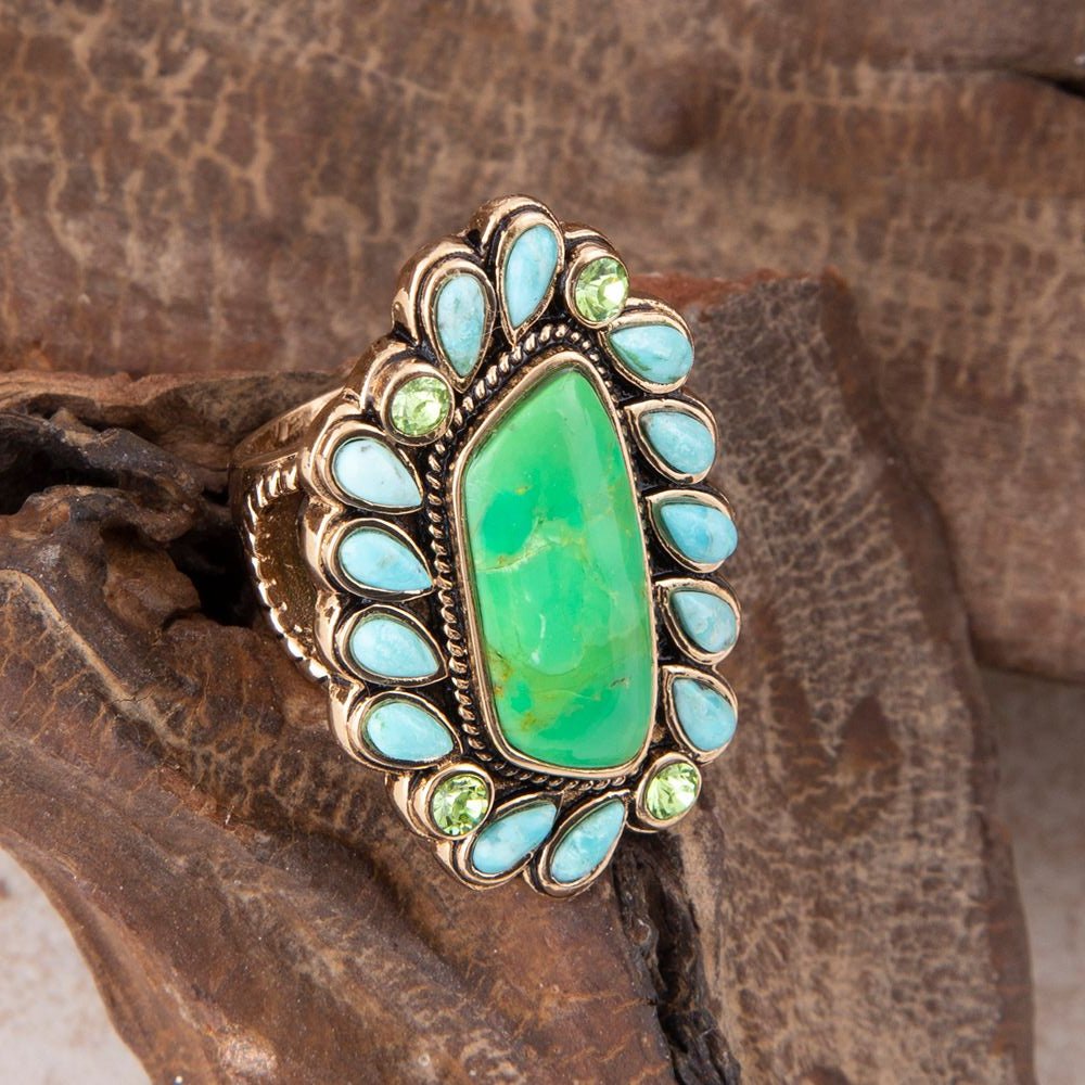 Ring with green gemstone and turquoise stones on a wooden background