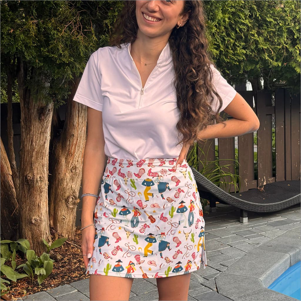Woman wearing a white polo shirt and colorful skirt with animal patterns outdoors.