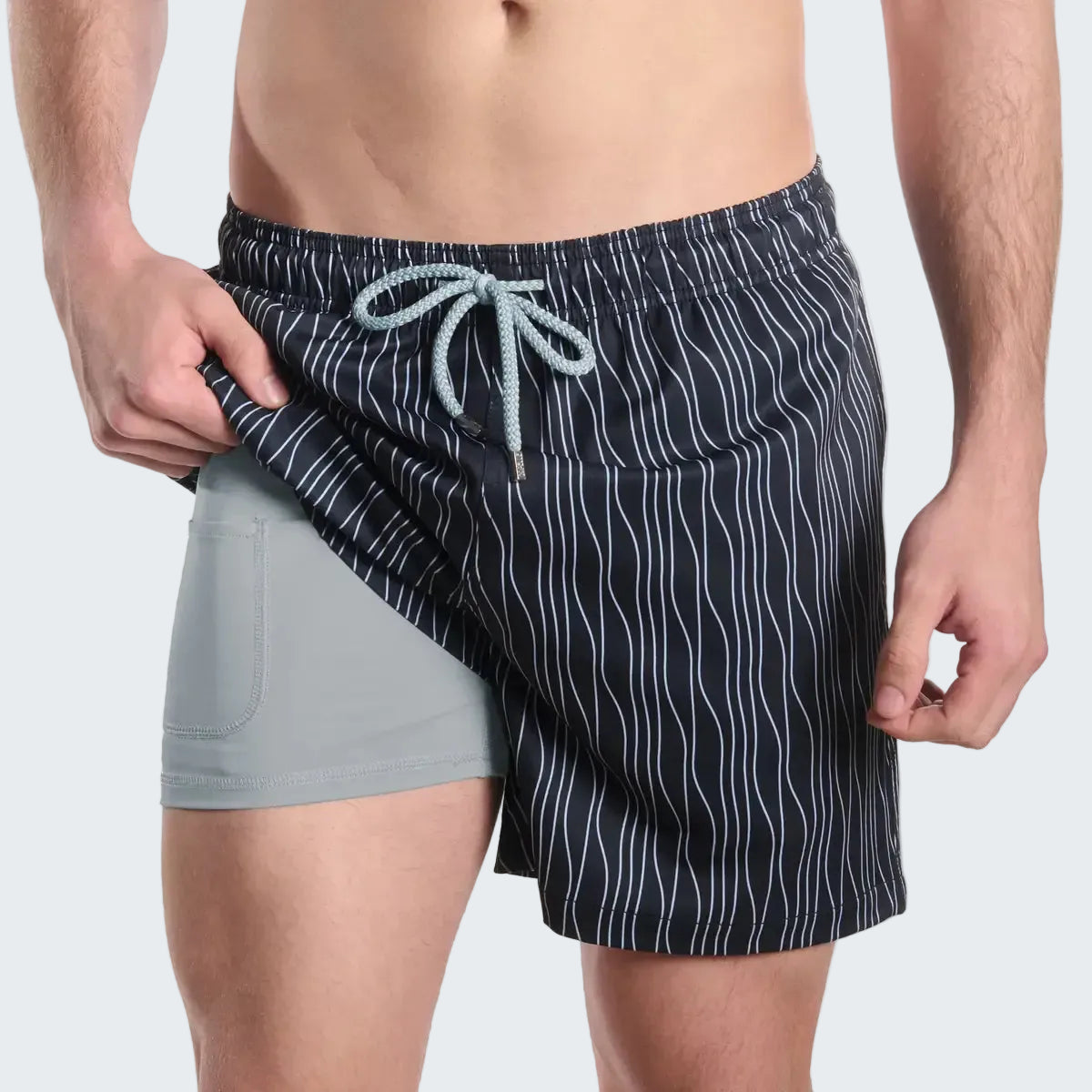 Person wearing a black swim trunks with white stripes on a white background