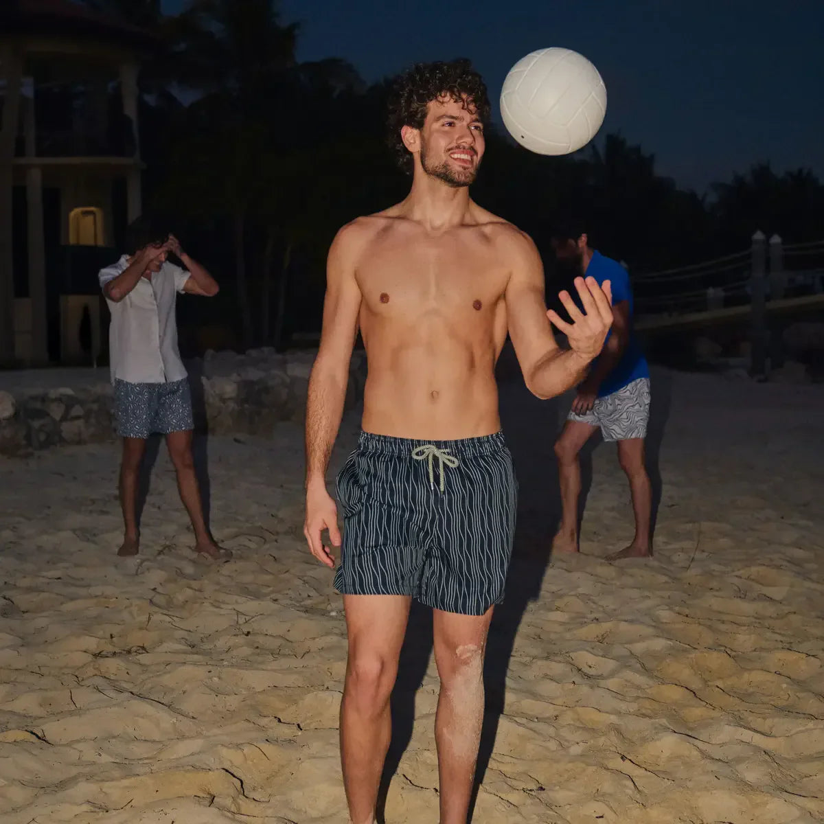 Man playing volleyball on a beach at night with palm trees in the background