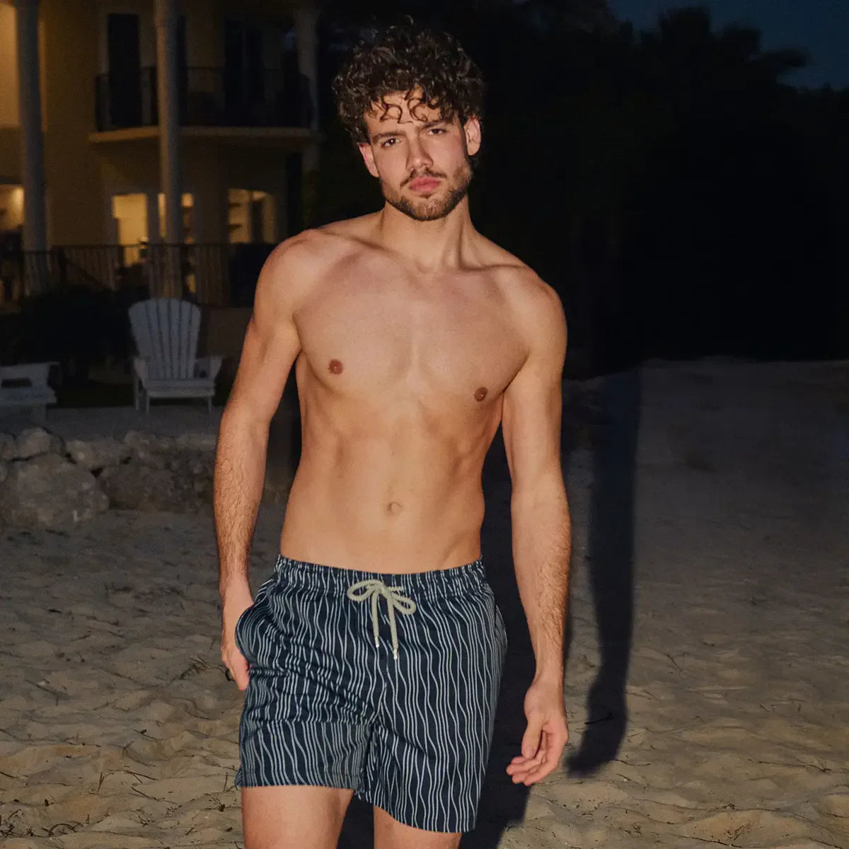 Man wearing striped swim shorts on a beach at night