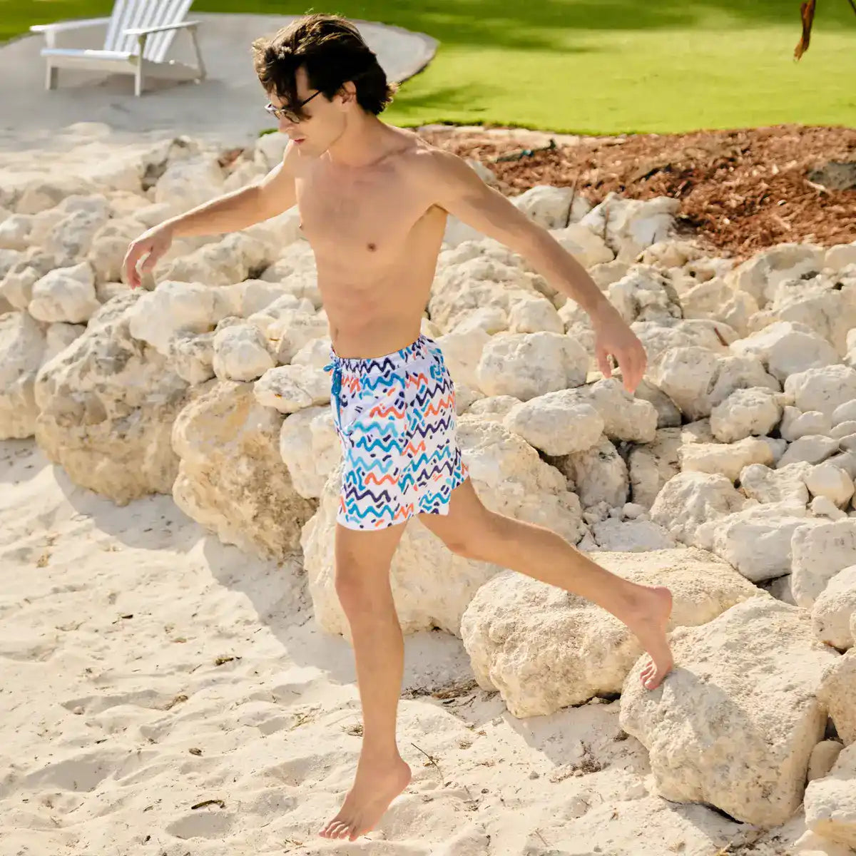 Man in colorful swim shorts walking on a rocky beach