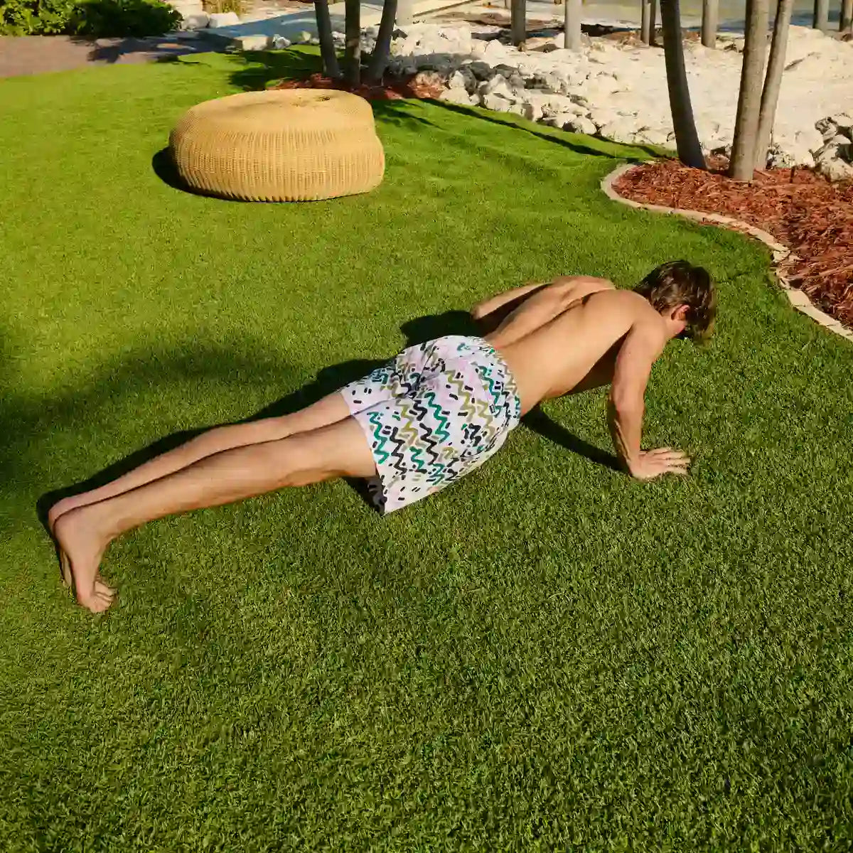 Person doing push-ups on grass wearing patterned shorts