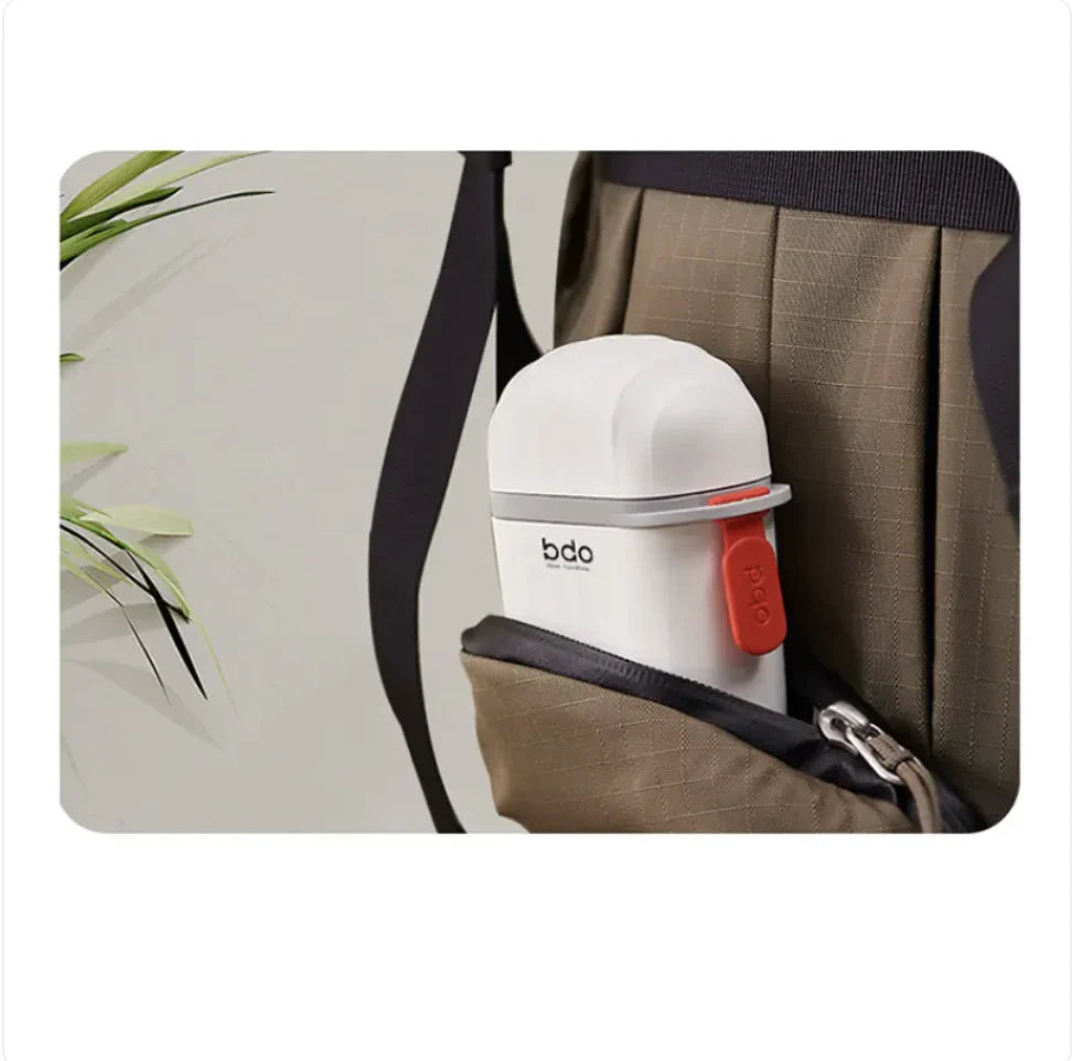 White container with red lid labeled 'bdo' in a brown bag with a plant in the background