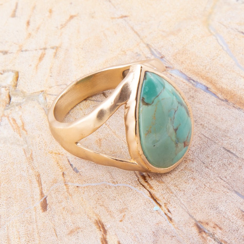Gold ring with a turquoise stone on a beige marble surface