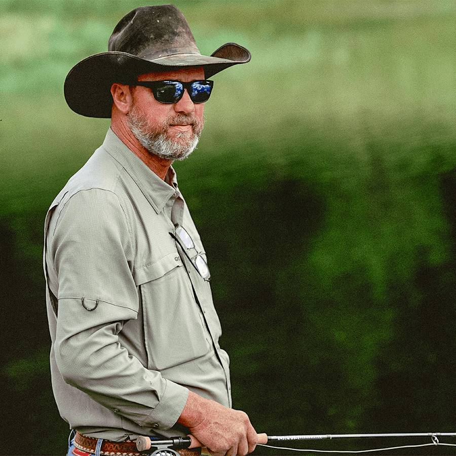 Man wearing a cowboy hat and sunglasses holding a bow and arrow with a green blurred background