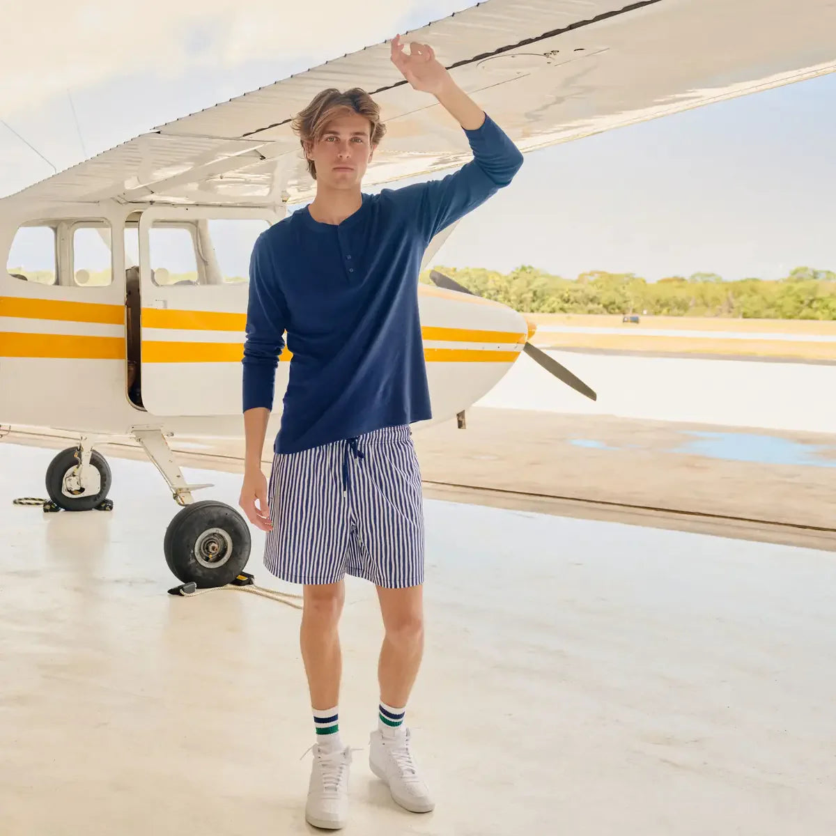 Man standing in front of a small airplane wearing a blue shirt and striped shorts.