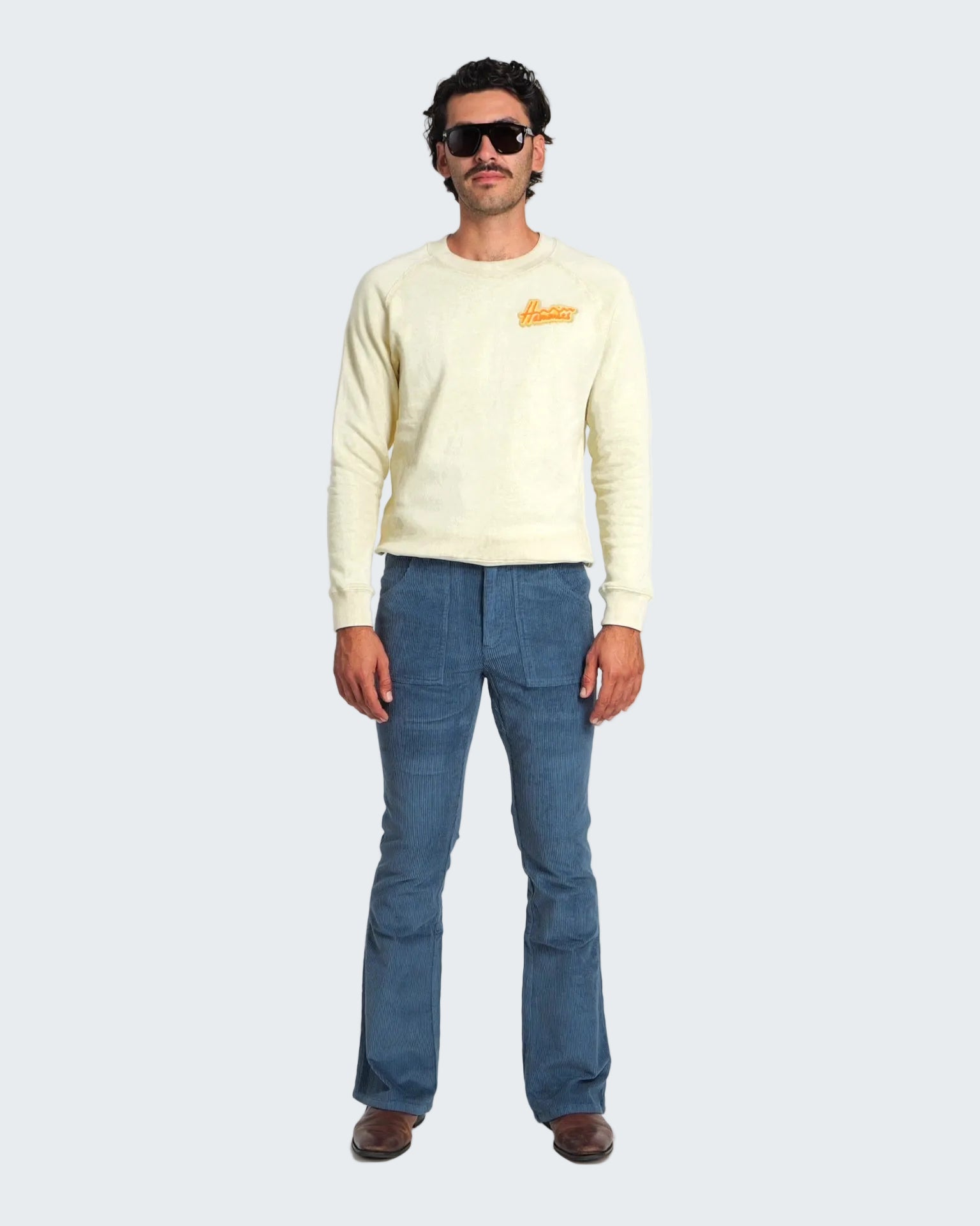 Man wearing a light-colored sweater and blue jeans on a white background
