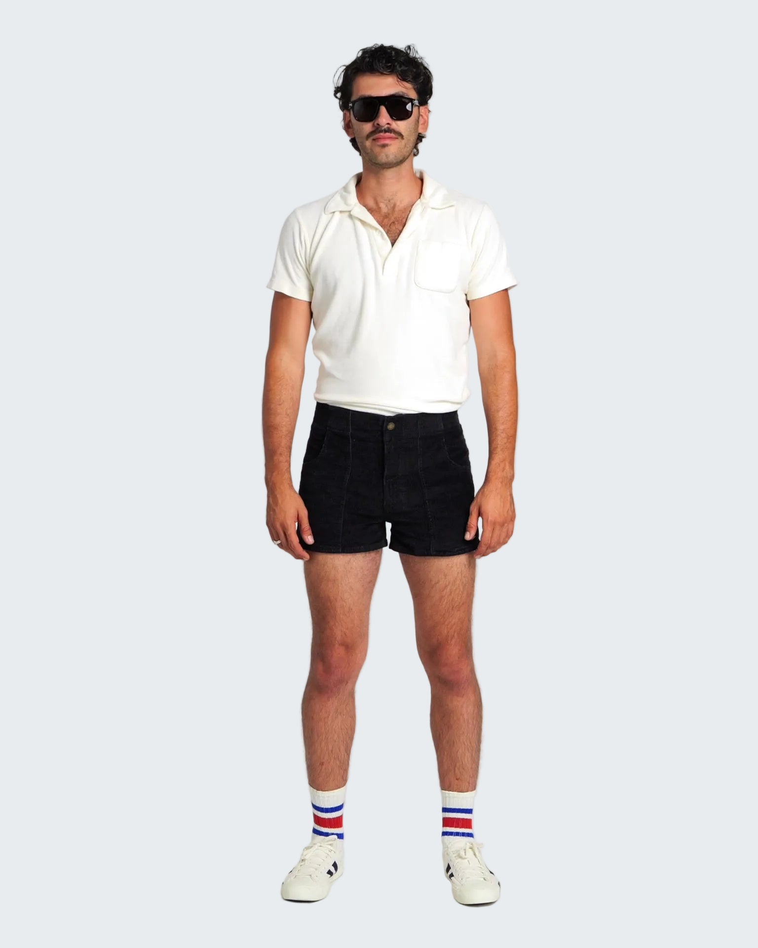Man wearing a white polo shirt, black shorts, and striped socks on a plain background