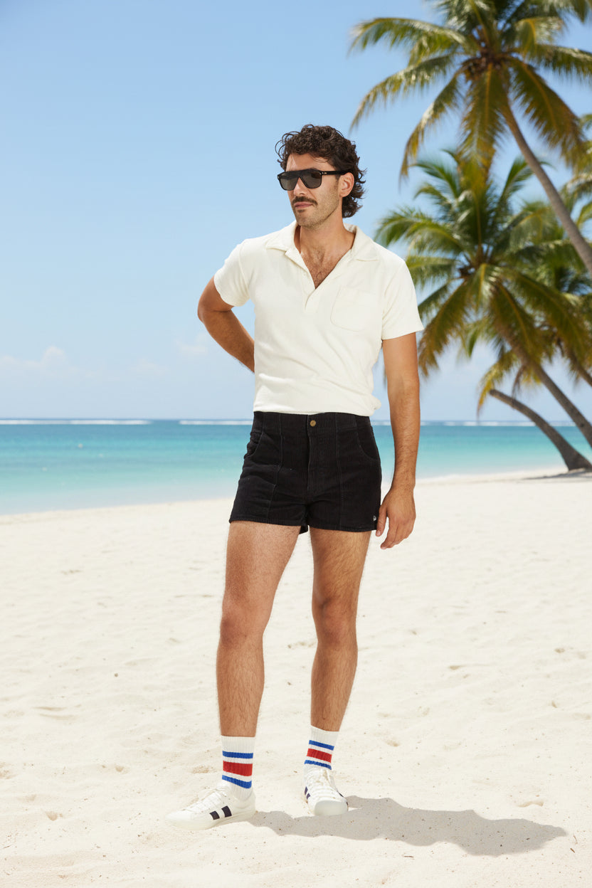 Man wearing a white polo shirt, black shorts, and striped socks on a white background