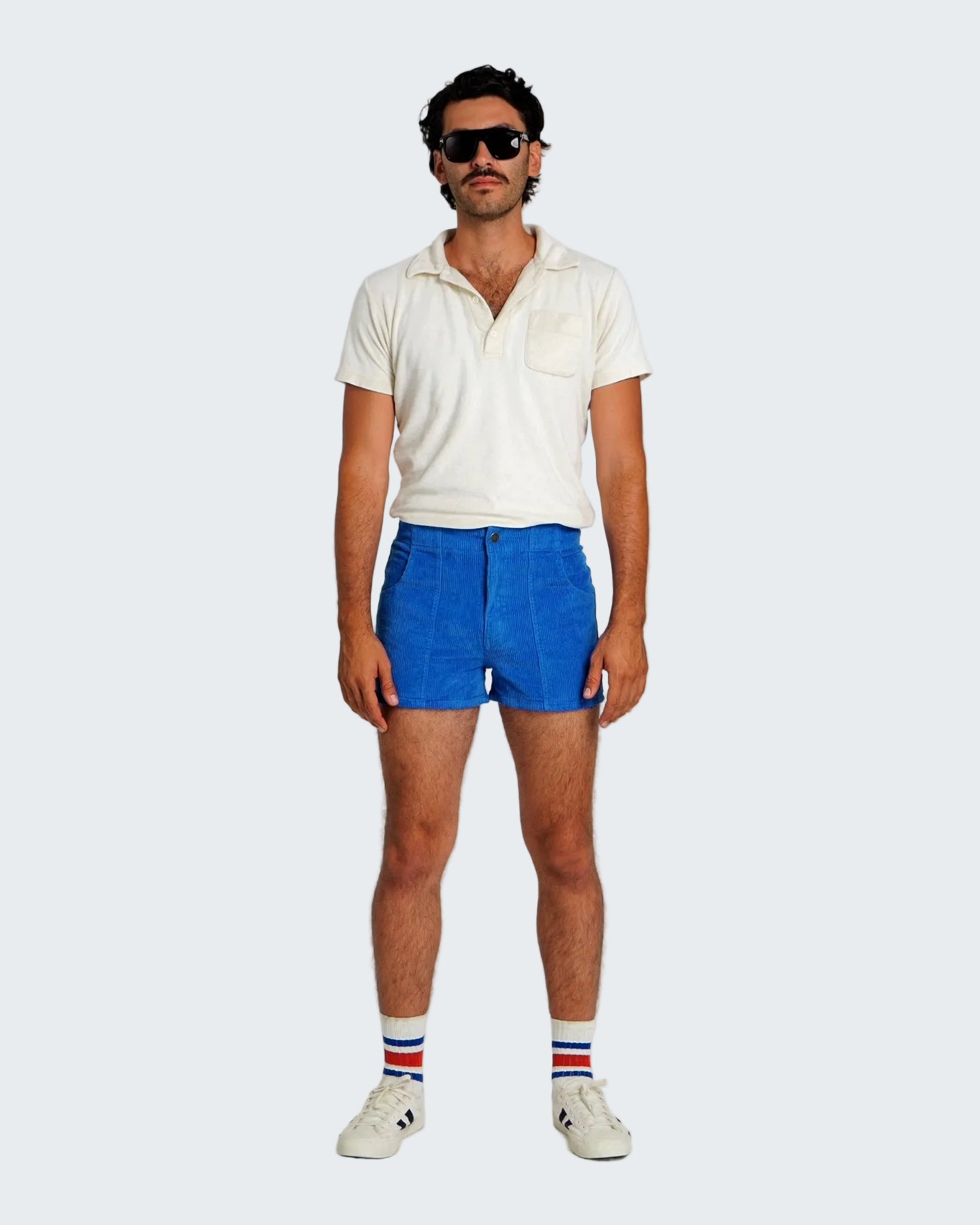 Man wearing a white shirt, blue shorts, and striped socks on a plain background