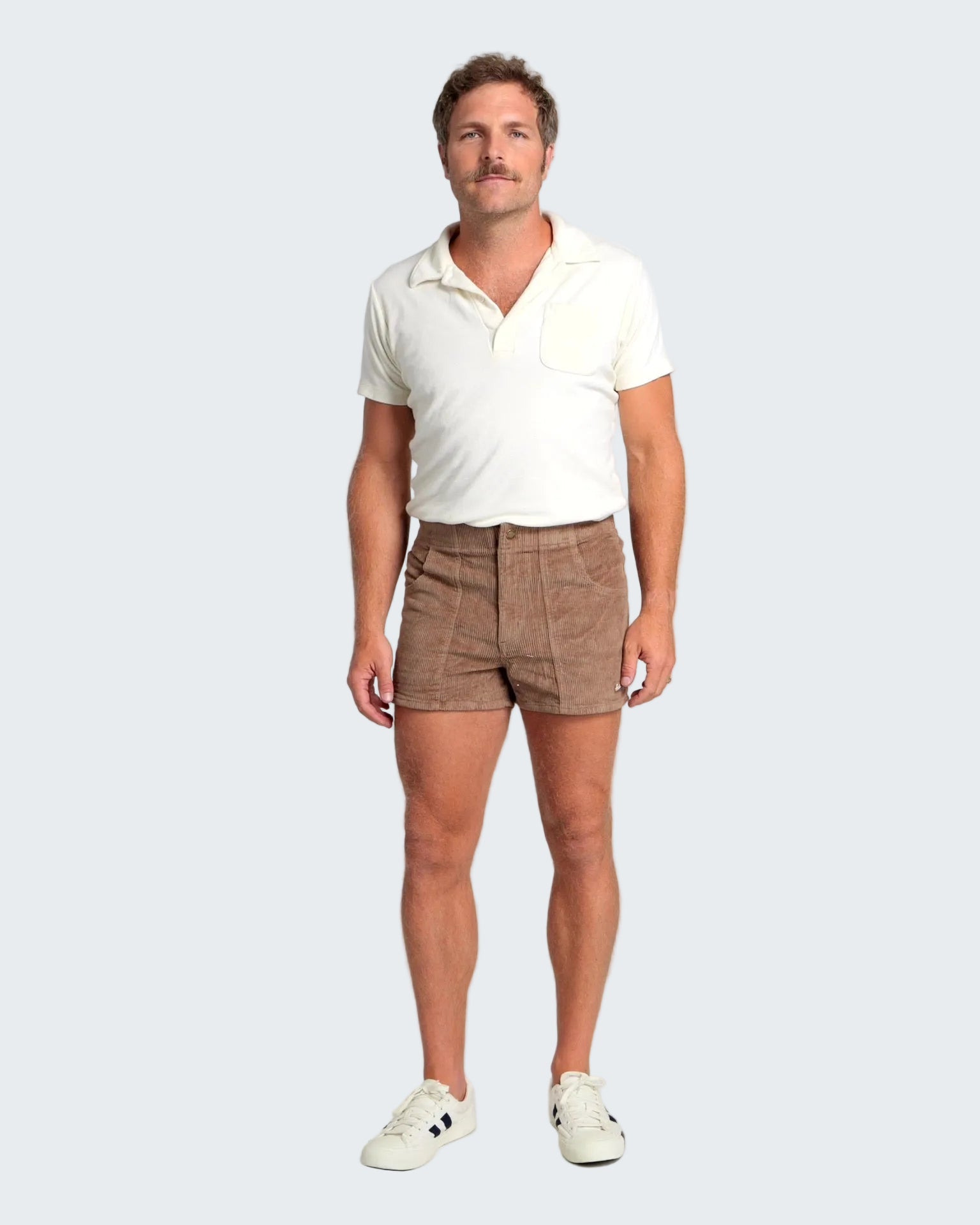 Man wearing a white polo shirt and brown shorts on a plain background