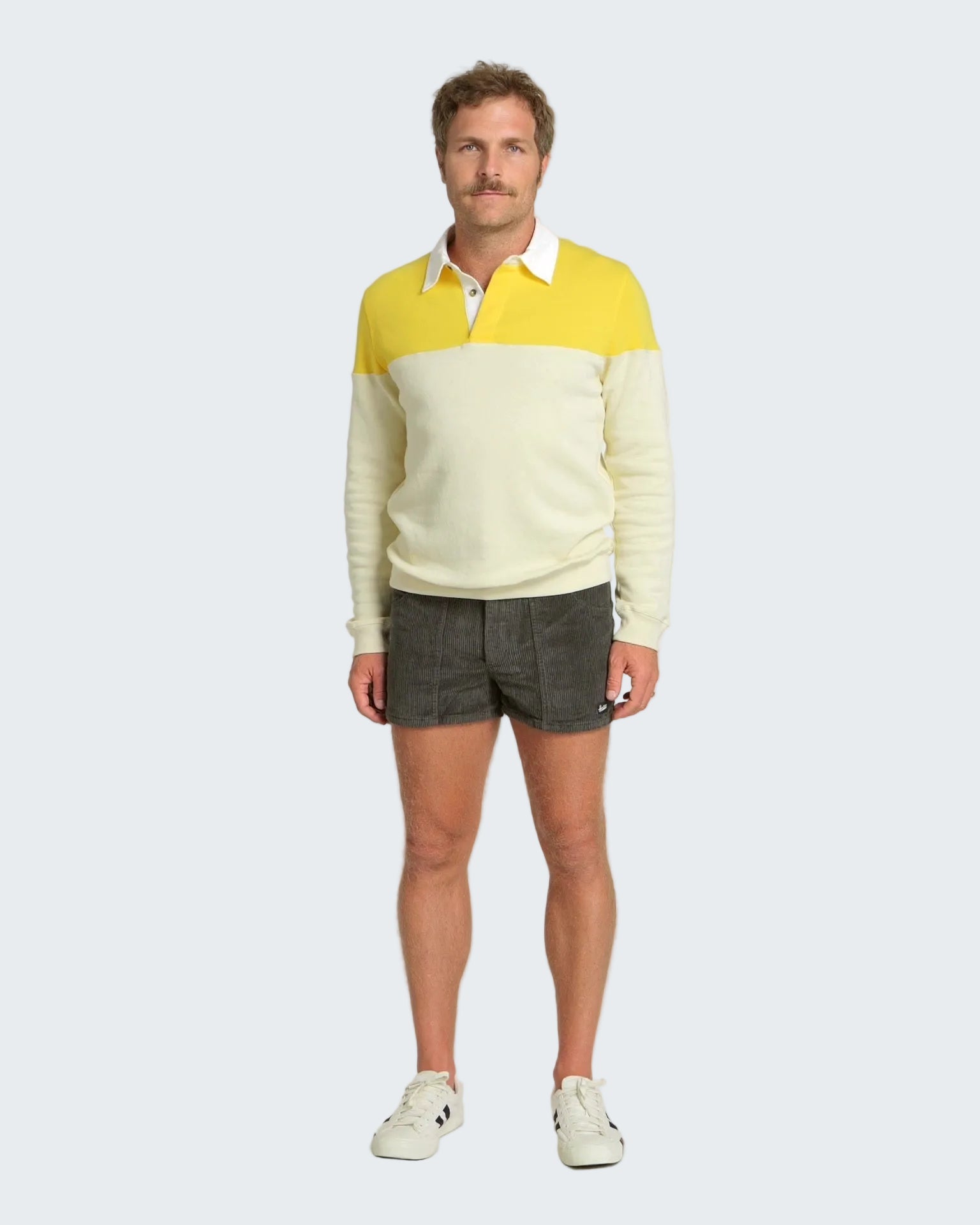 Man wearing a two-tone sweater with yellow and white, paired with dark shorts on a white background