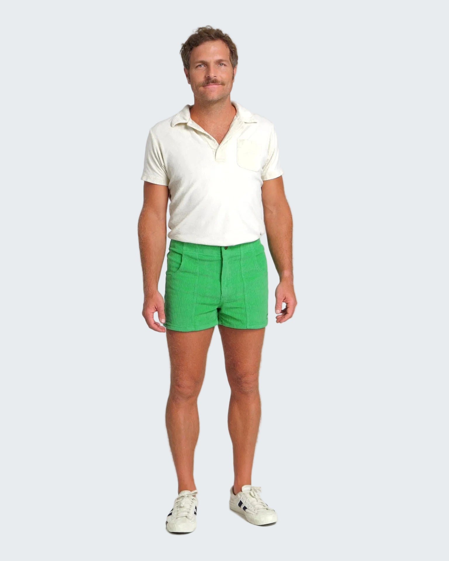 Man wearing a white polo shirt and green shorts on a plain background