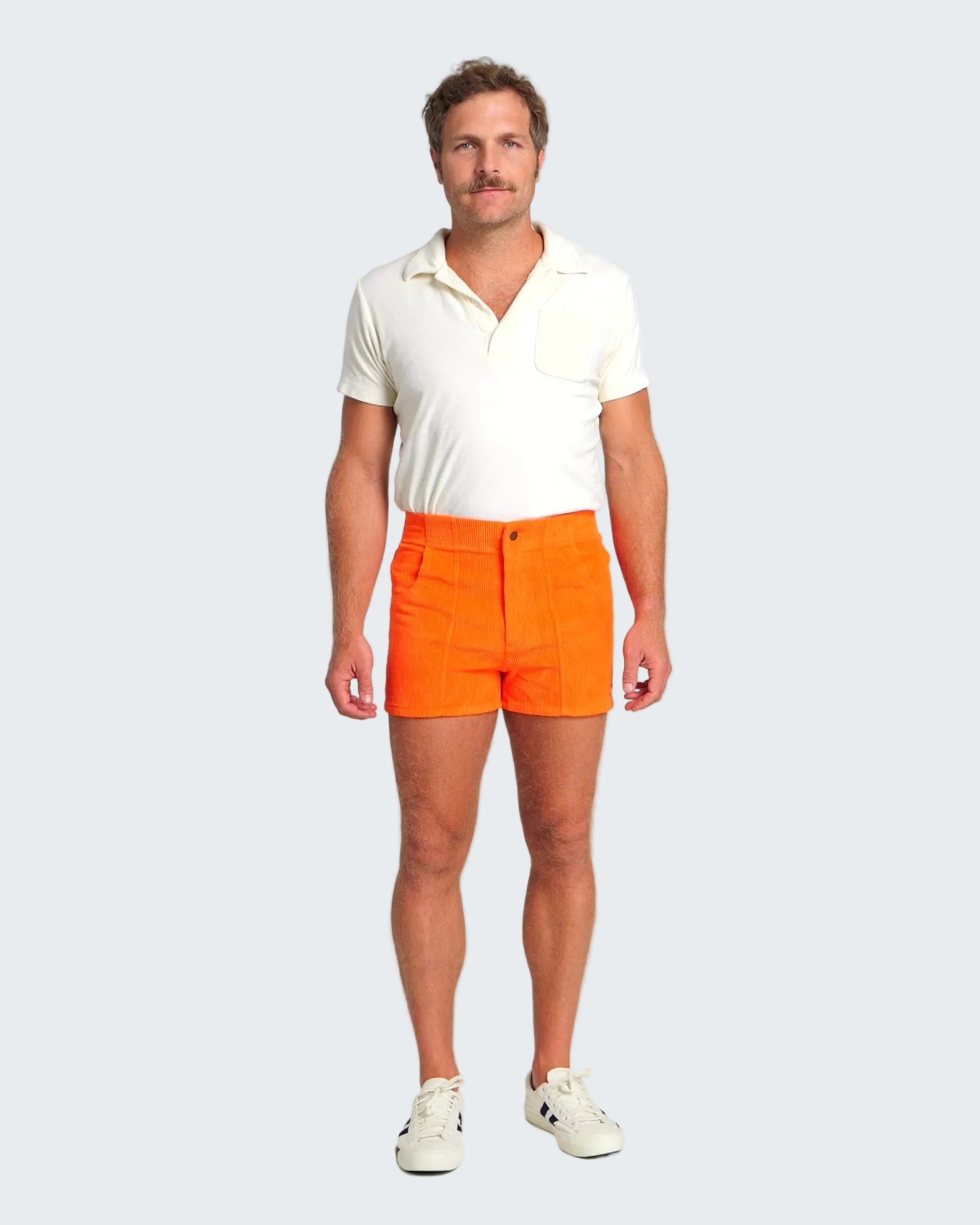 Man wearing a white polo shirt and bright orange shorts on a white background