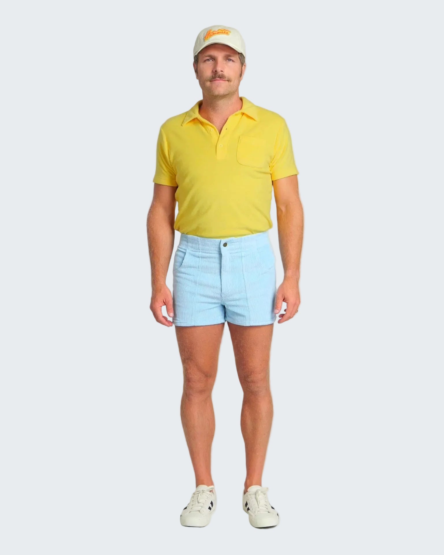 Man wearing a yellow polo shirt, light blue shorts, and a white cap on a white background