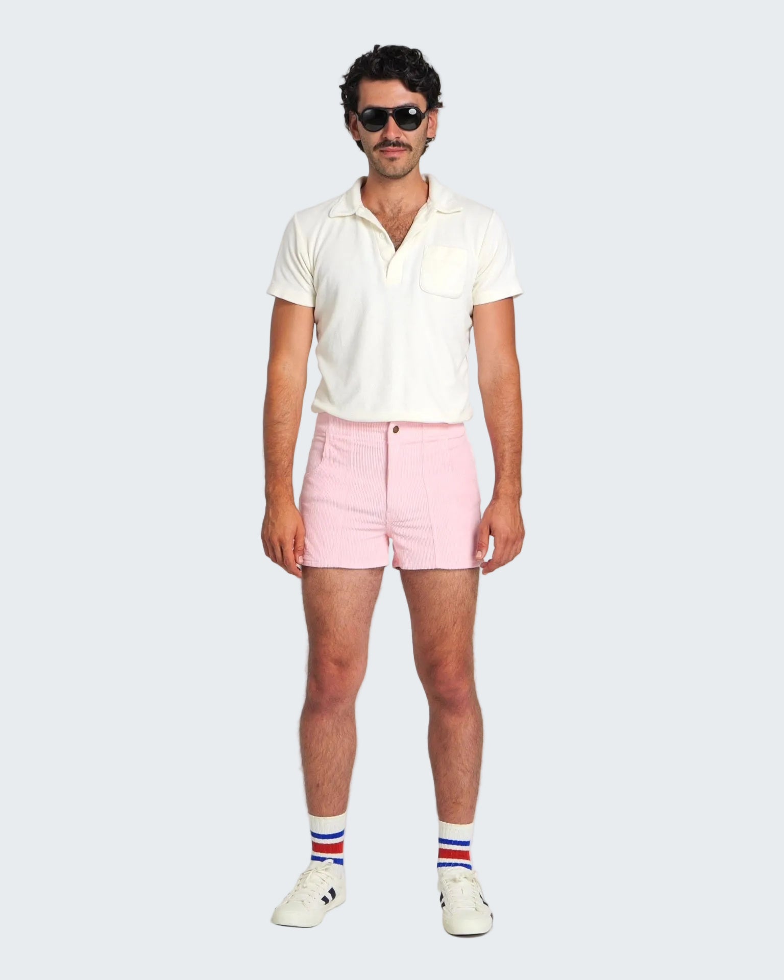 Man wearing a white polo shirt, pink shorts, and striped socks on a white background