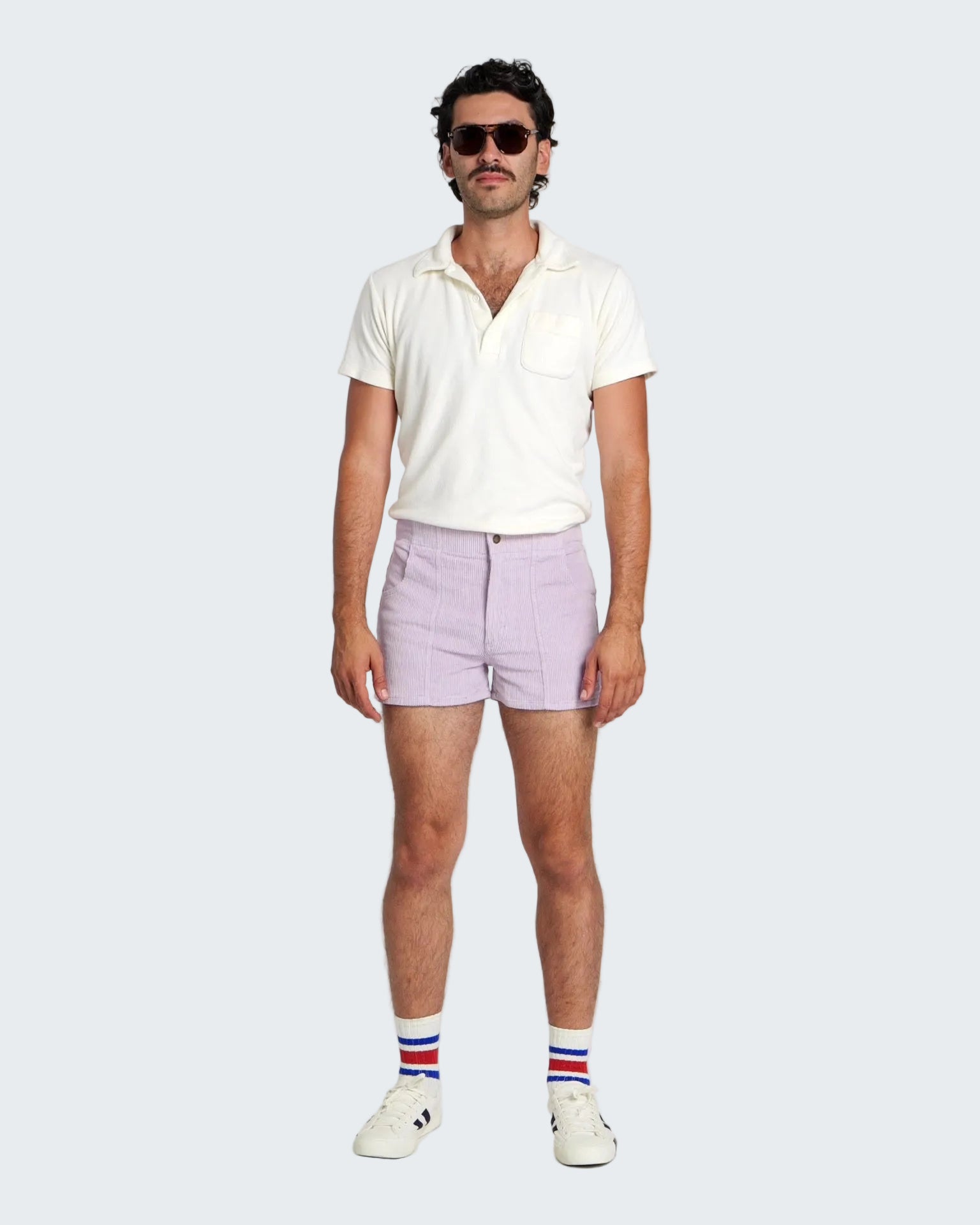 Man wearing a white polo shirt, light purple shorts, and striped socks on a white background