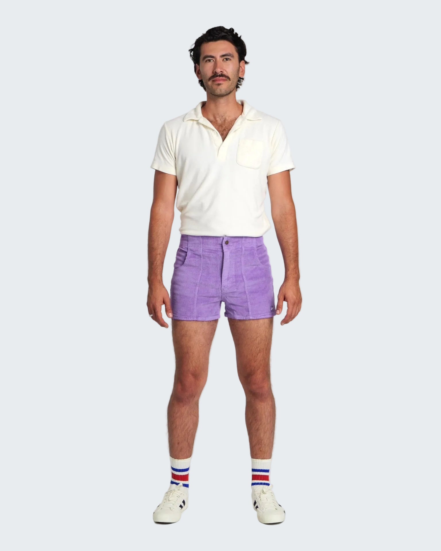 Man wearing a white polo shirt, purple shorts, and striped socks on a white background