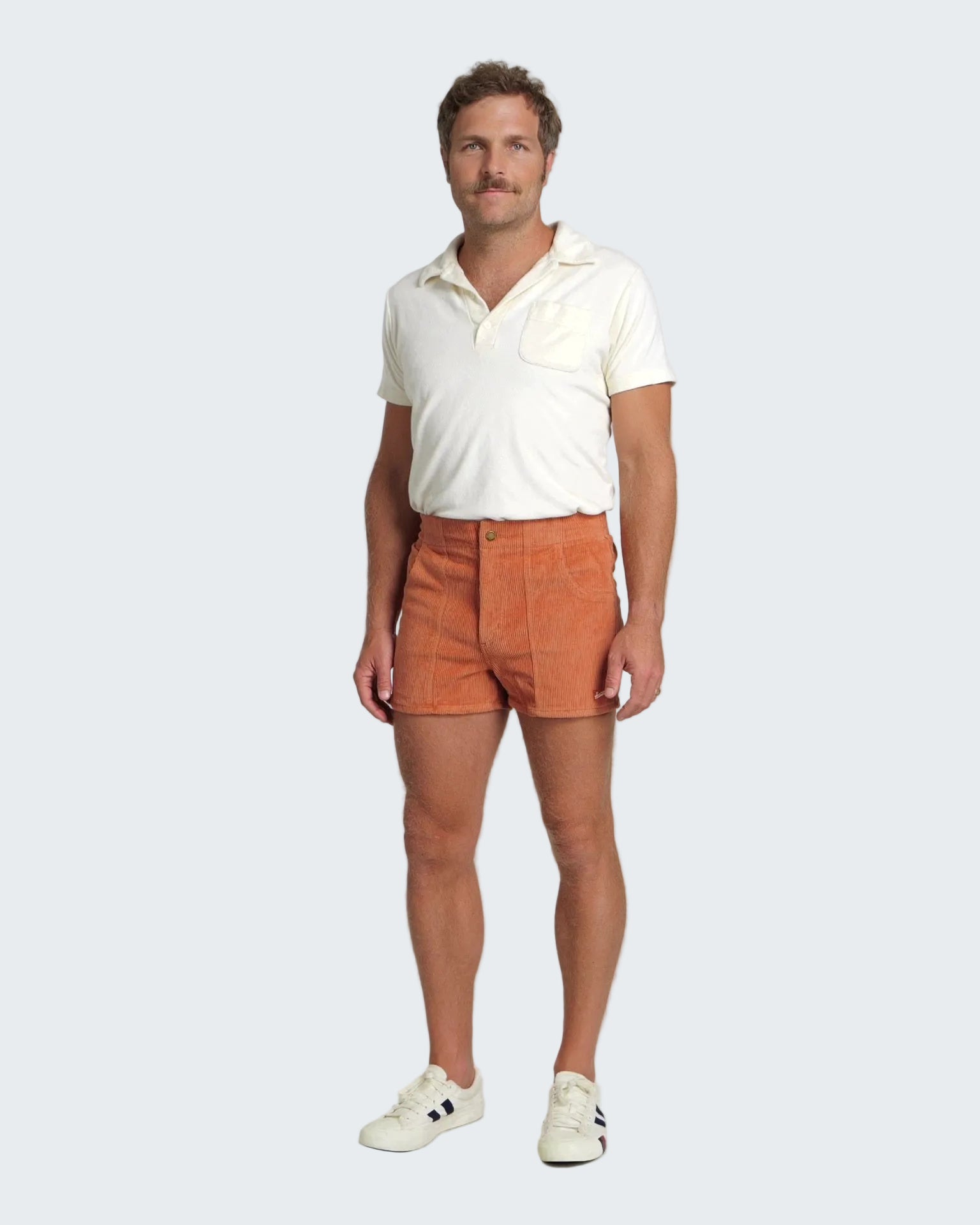 Man wearing a white polo shirt and orange shorts on a white background