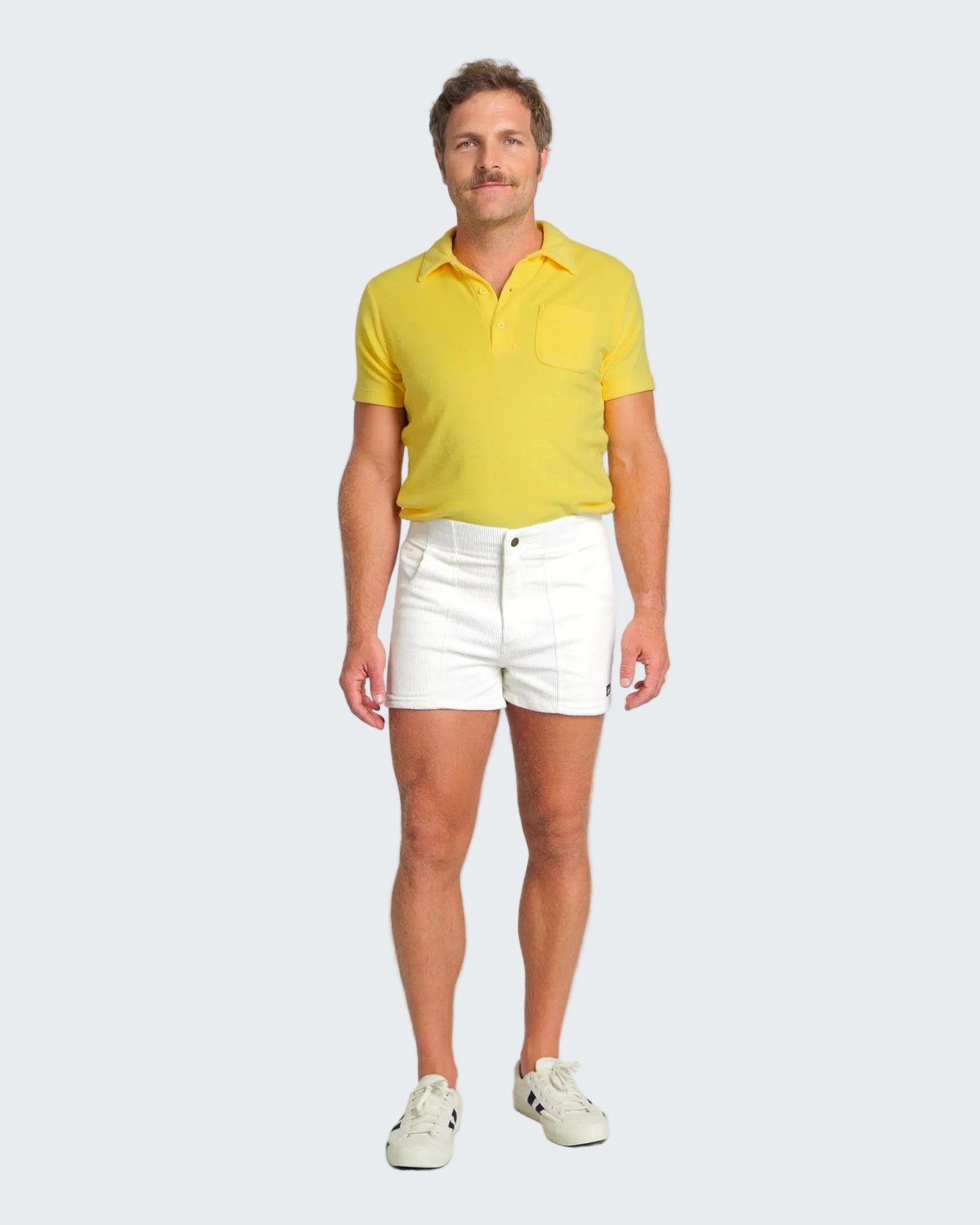 Man wearing a yellow polo shirt and white shorts on a plain background