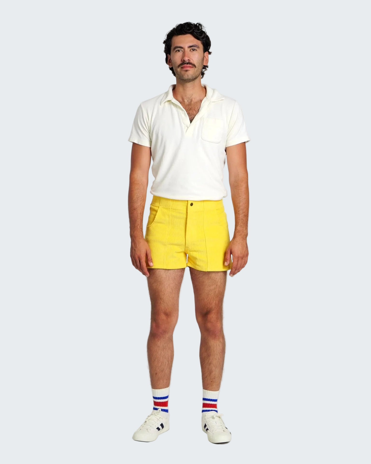 Man wearing a white polo shirt and yellow shorts with a plain background