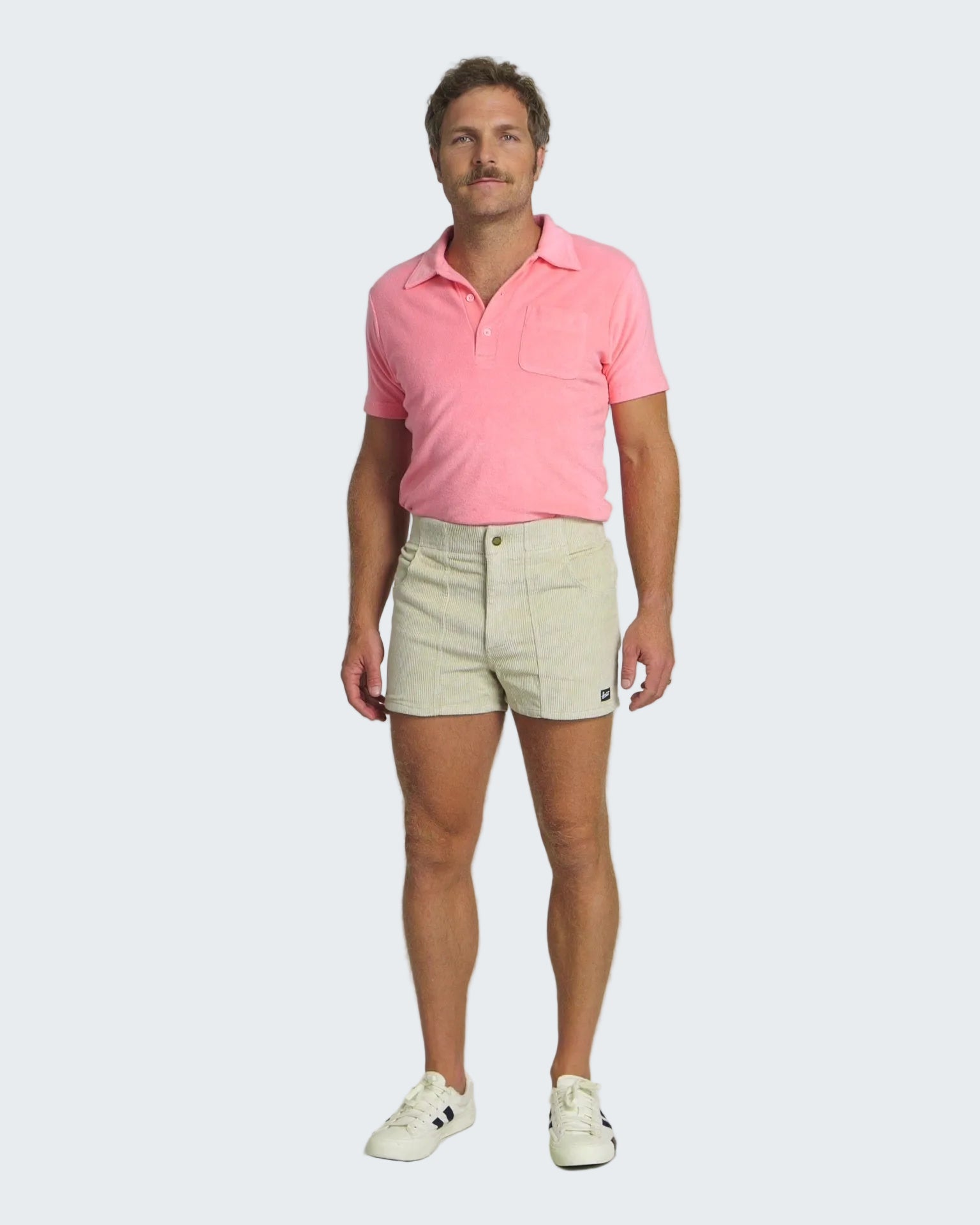Man wearing a pink polo shirt and beige shorts on a white background