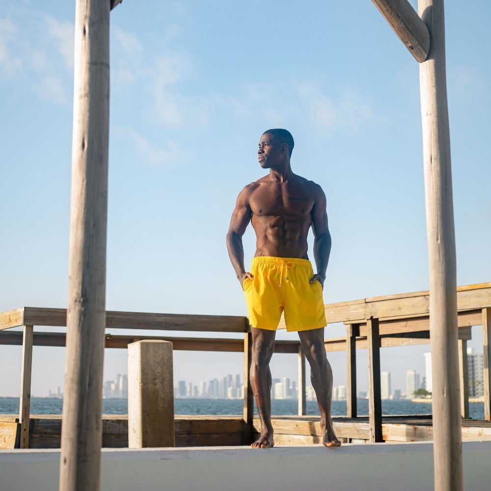 Man in yellow shorts standing on a wooden platform with a city skyline in the background