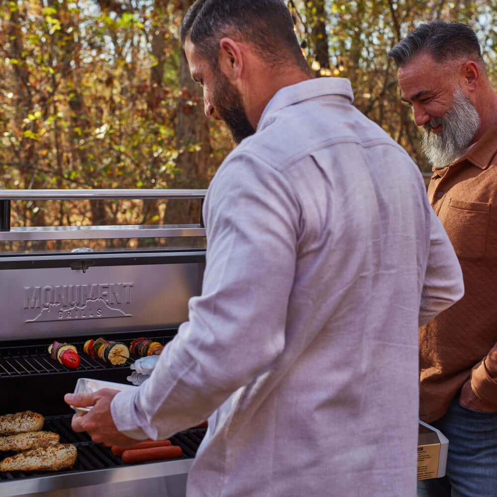 Two men grilling outdoors with a Moenvent Grill in the background