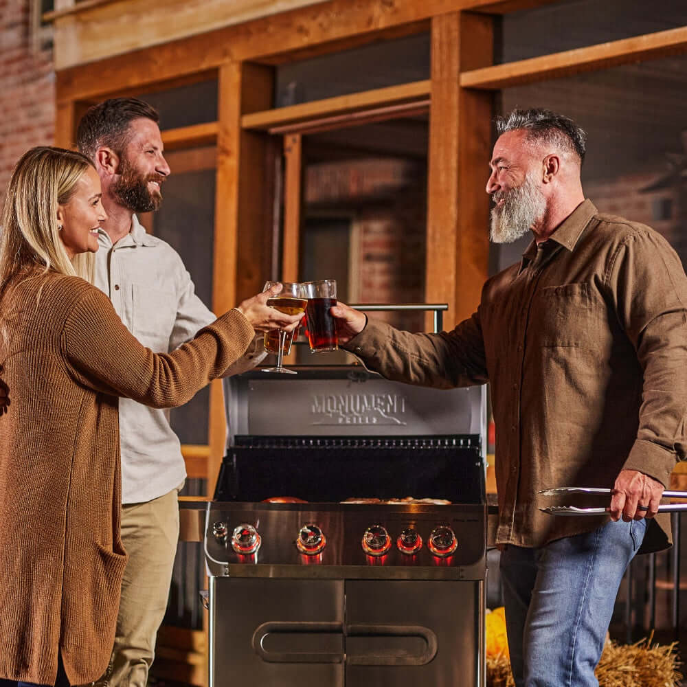 Three people toasting with drinks in front of a Monogram grill.