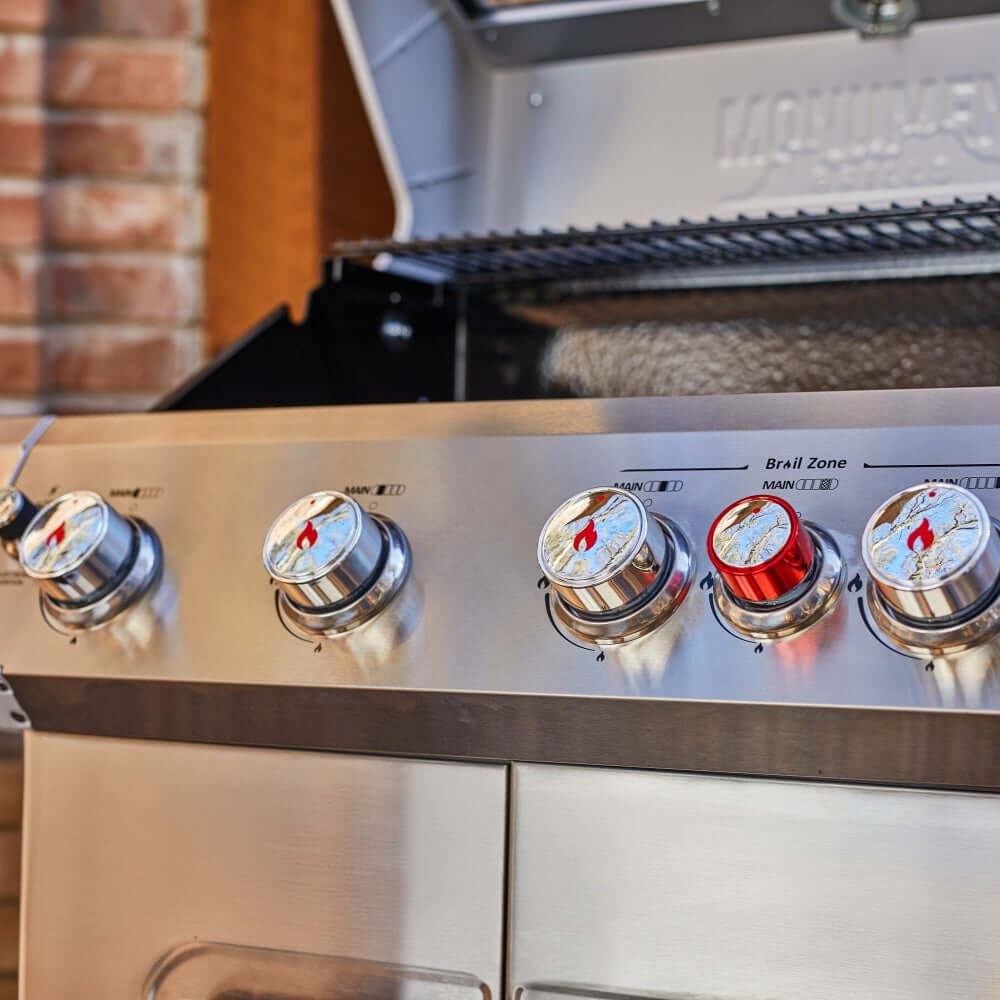 Close-up of a stainless steel grill with control knobs against a brick wall.