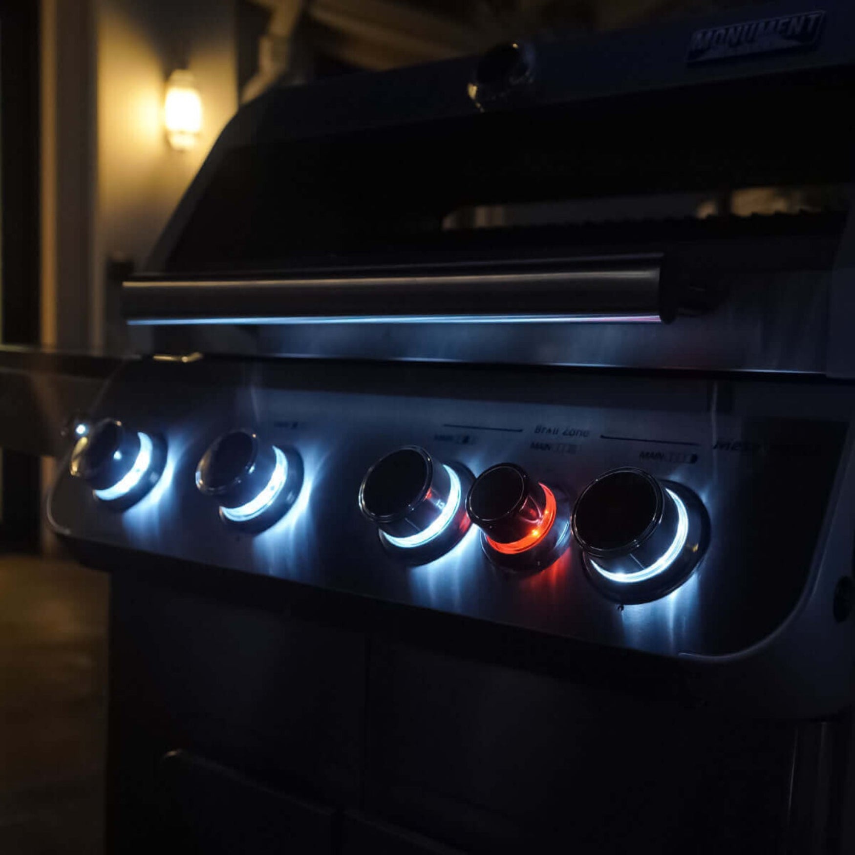 Close-up of a grill with glowing control knobs in a dimly lit setting