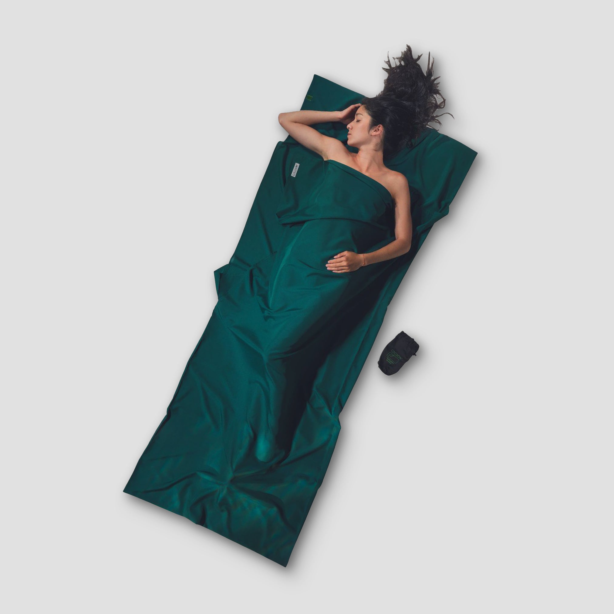 Person lying on a green sleeping bag with a black sleeping pad on a white background