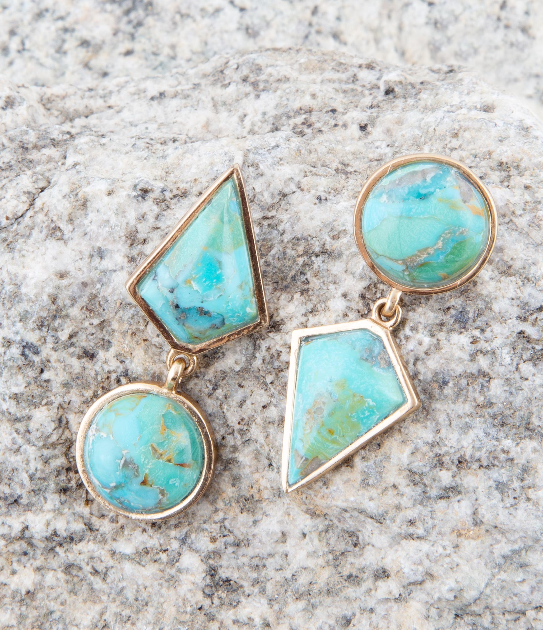 Turquoise stone earrings with gold accents on a gray stone surface