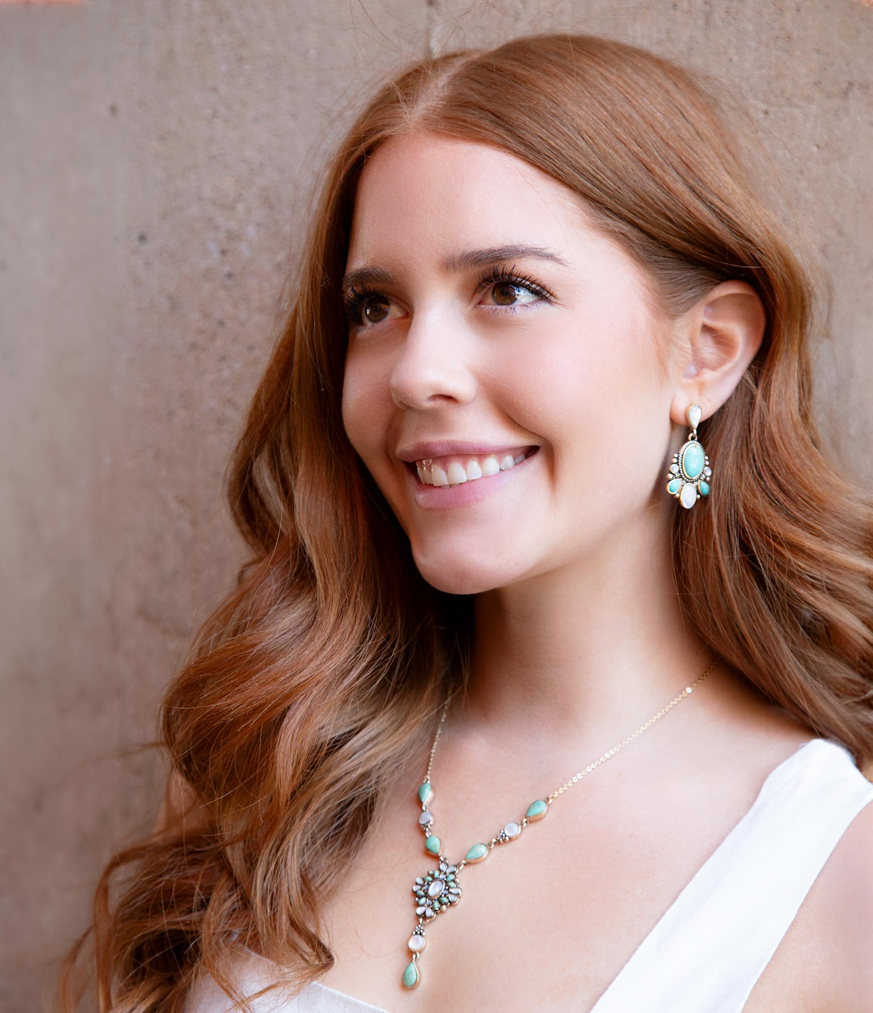 Woman wearing turquoise earrings and necklace against a neutral background