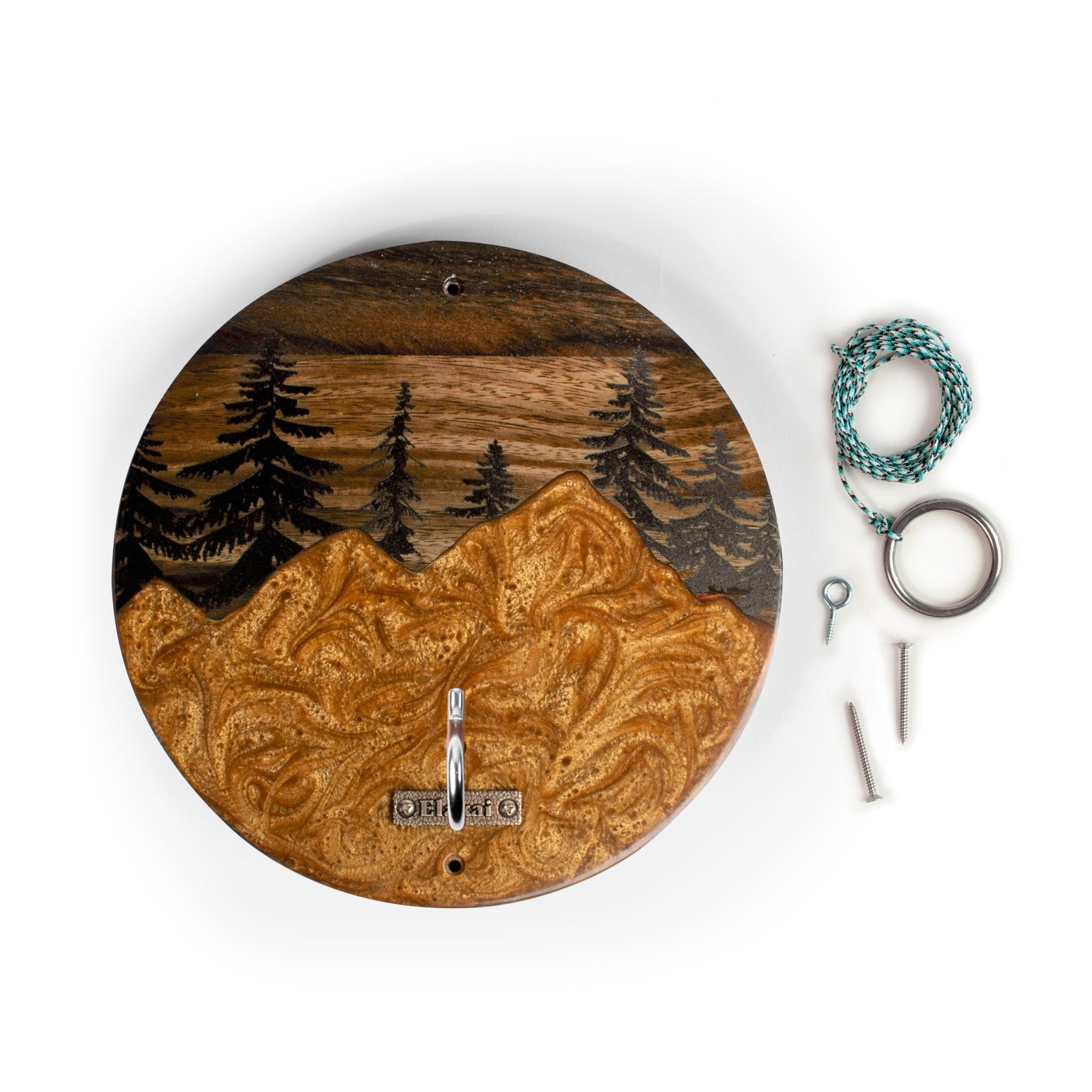 Round wooden wall clock with an engraved mountain and pine tree landscape, shown with mounting hardware including a teal cord, metal ring, and screws on a white background.