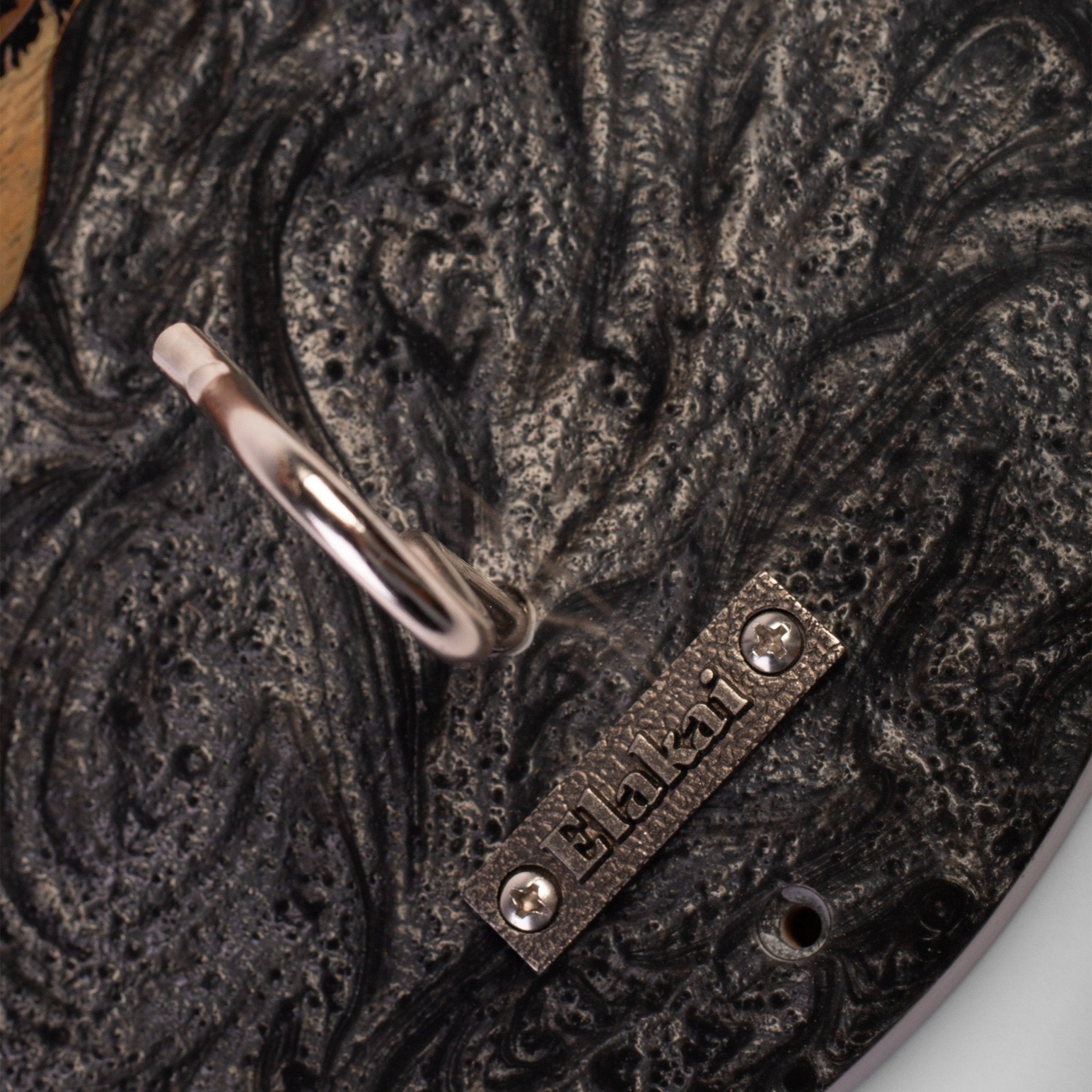 Close-up of a dark textured wall hook with a rectangular metal brand plate reading ELKZAR.