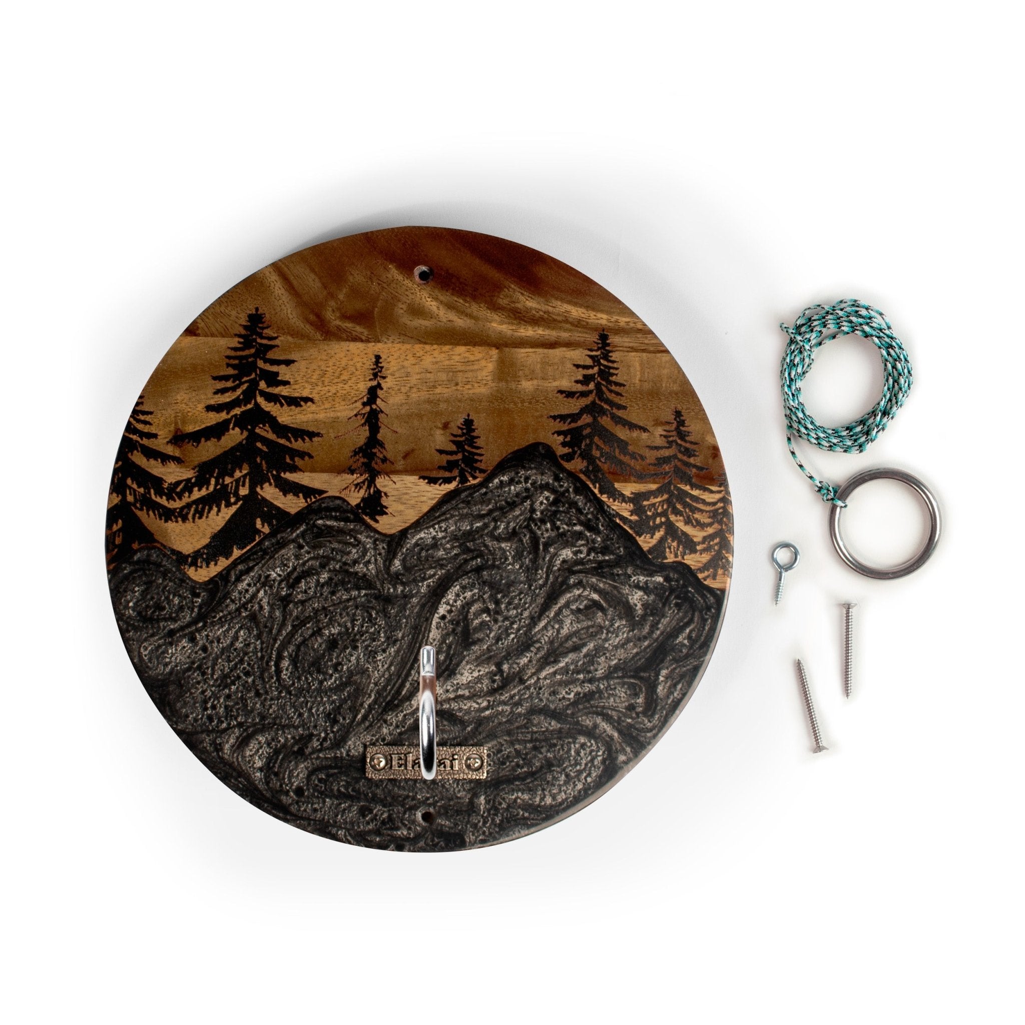 Round wooden wall clock with an engraved mountain and pine tree landscape, shown on a white background with mounting hardware and a hanging cord.