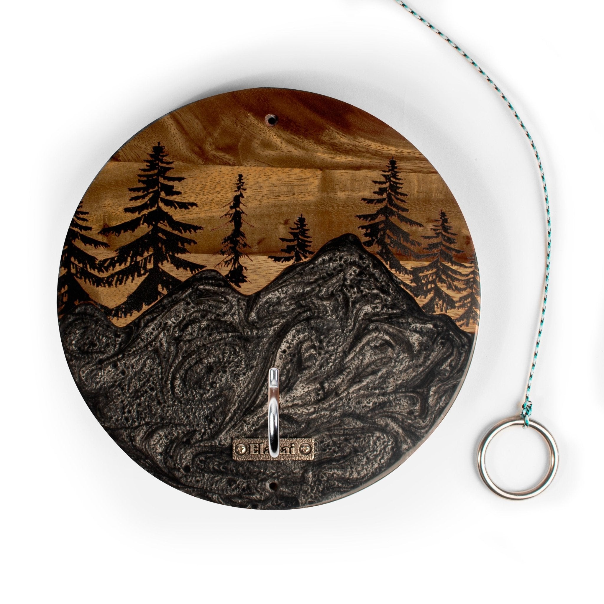 A round wooden mountain landscape ornament with a carved pine tree forest and mountain design, featuring a silver hanging hook and a teal-and-white cord with a metal ring on a white background.