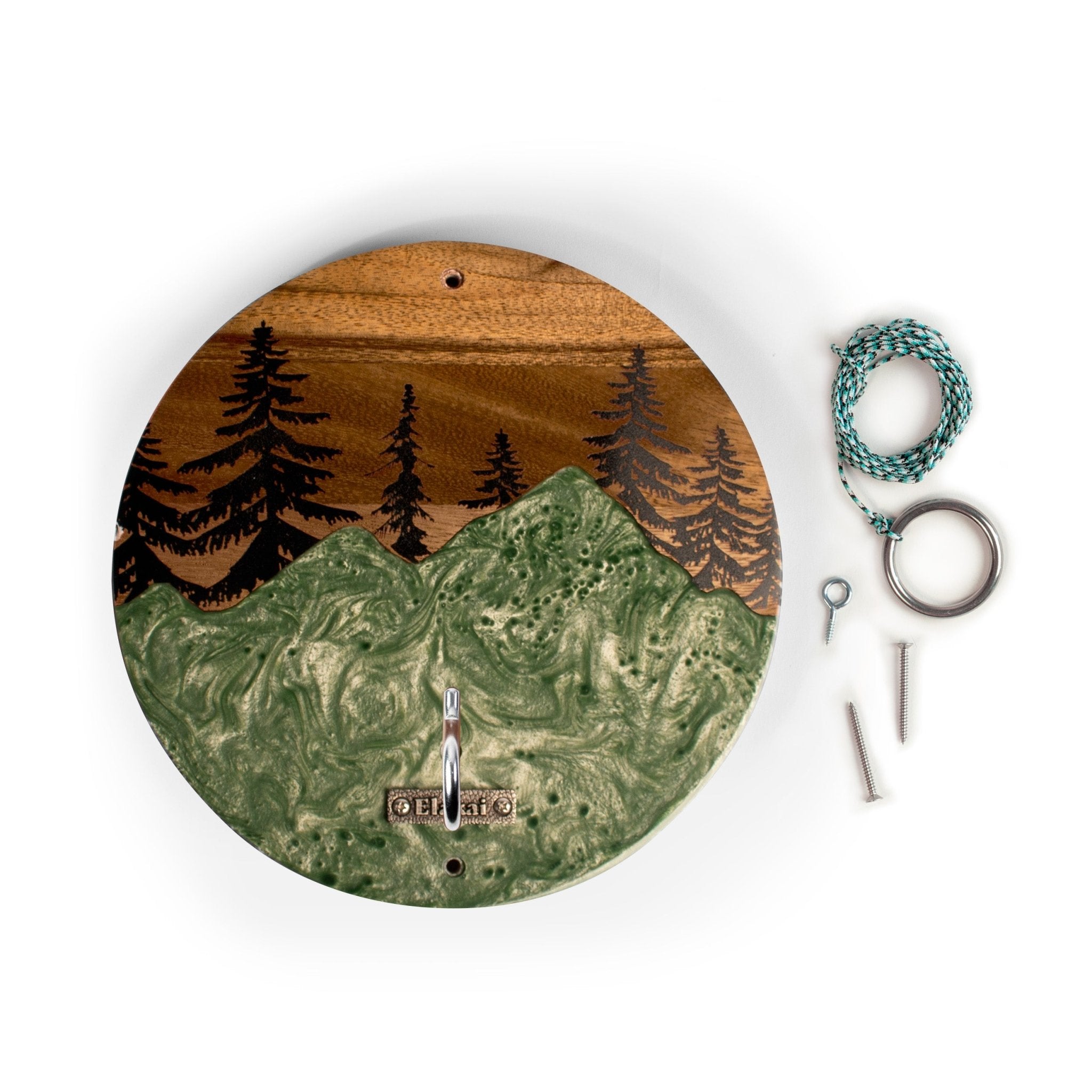Round wooden wall clock with an engraved mountain and pine tree landscape, shown with mounting hardware on a white background.