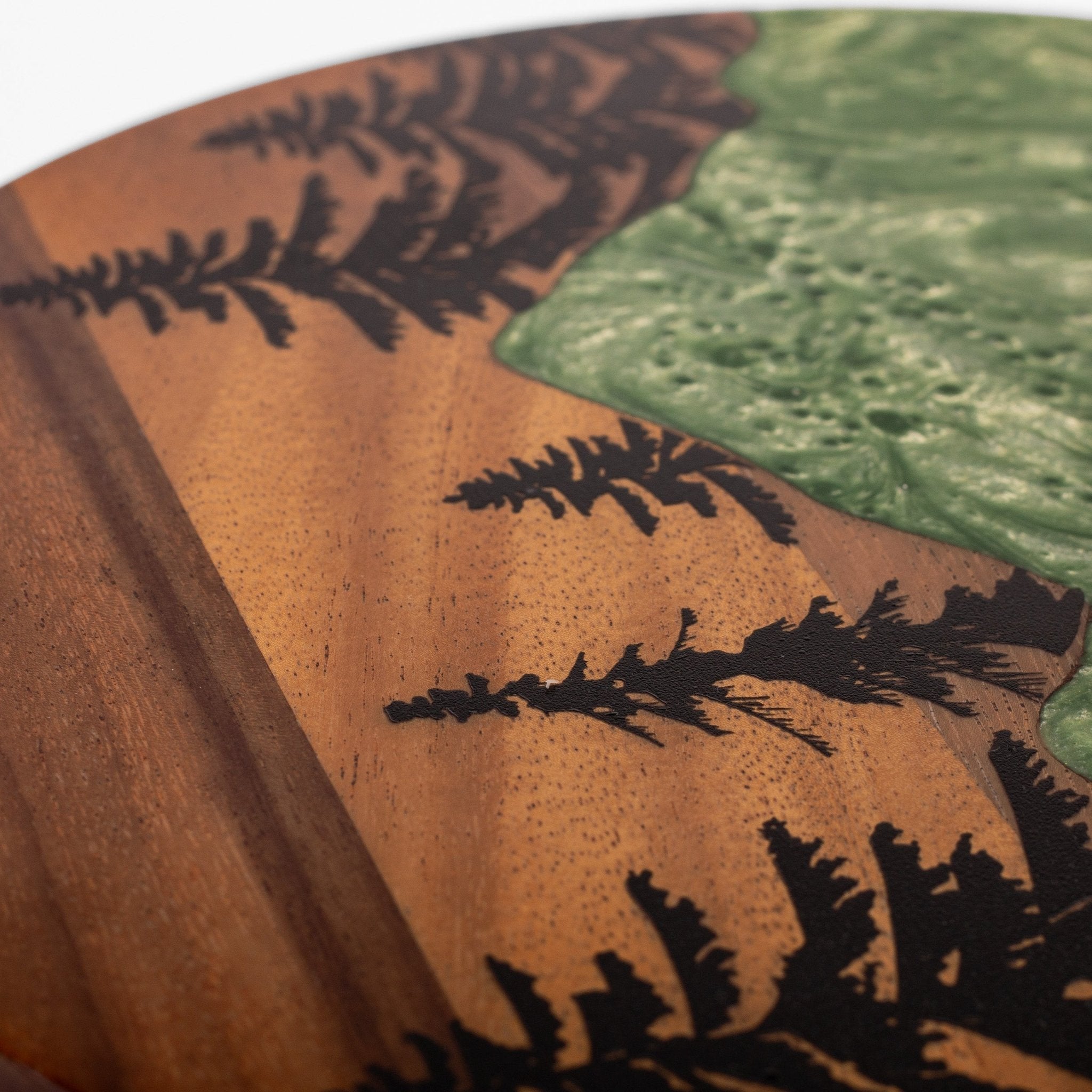 Close-up of a wooden decorative object featuring a natural wood grain base with black inlaid fern-like silhouettes and a green textured inlay.