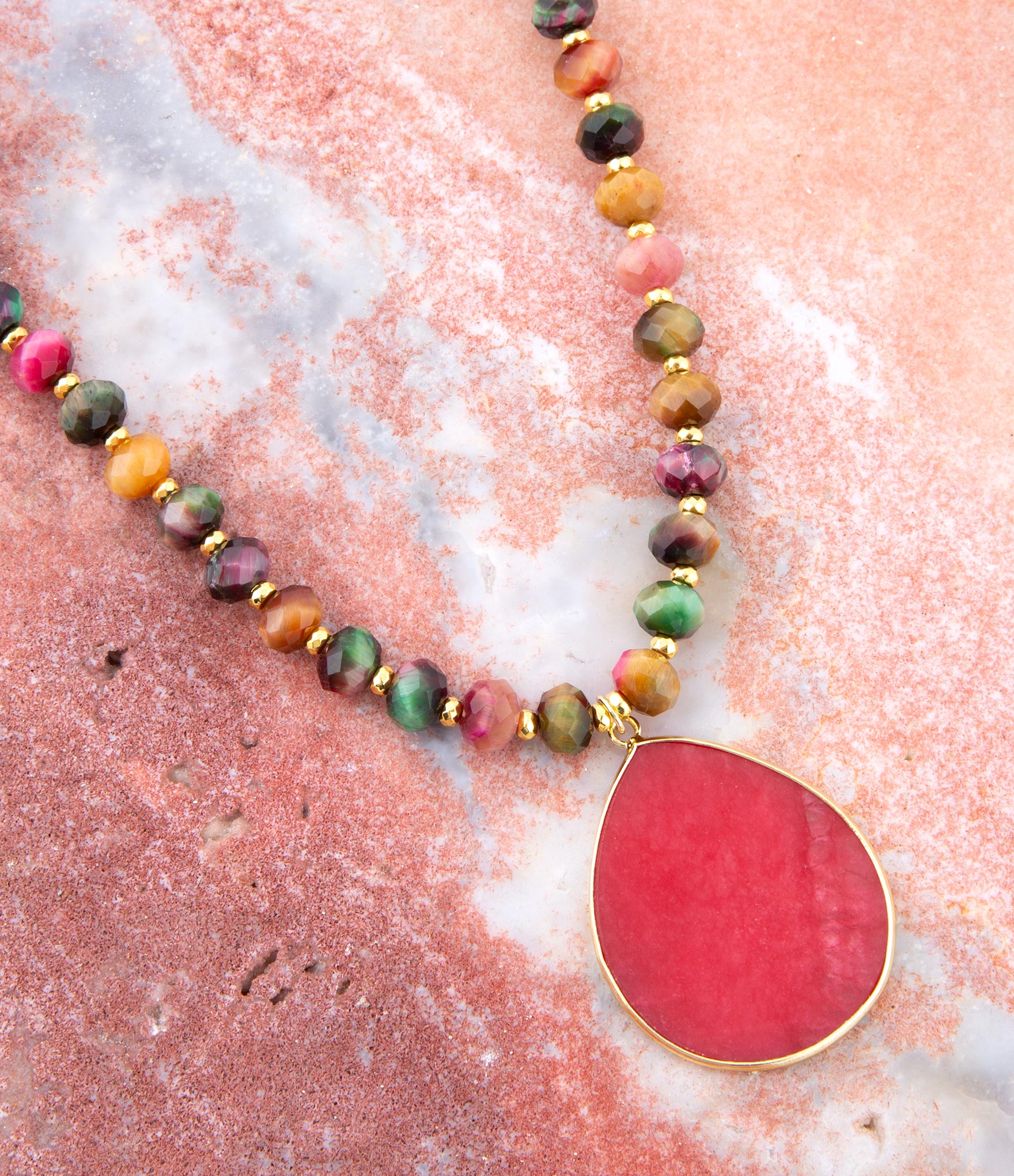 Necklace with multicolored beads and a large red pendant on a pink and white marbled surface