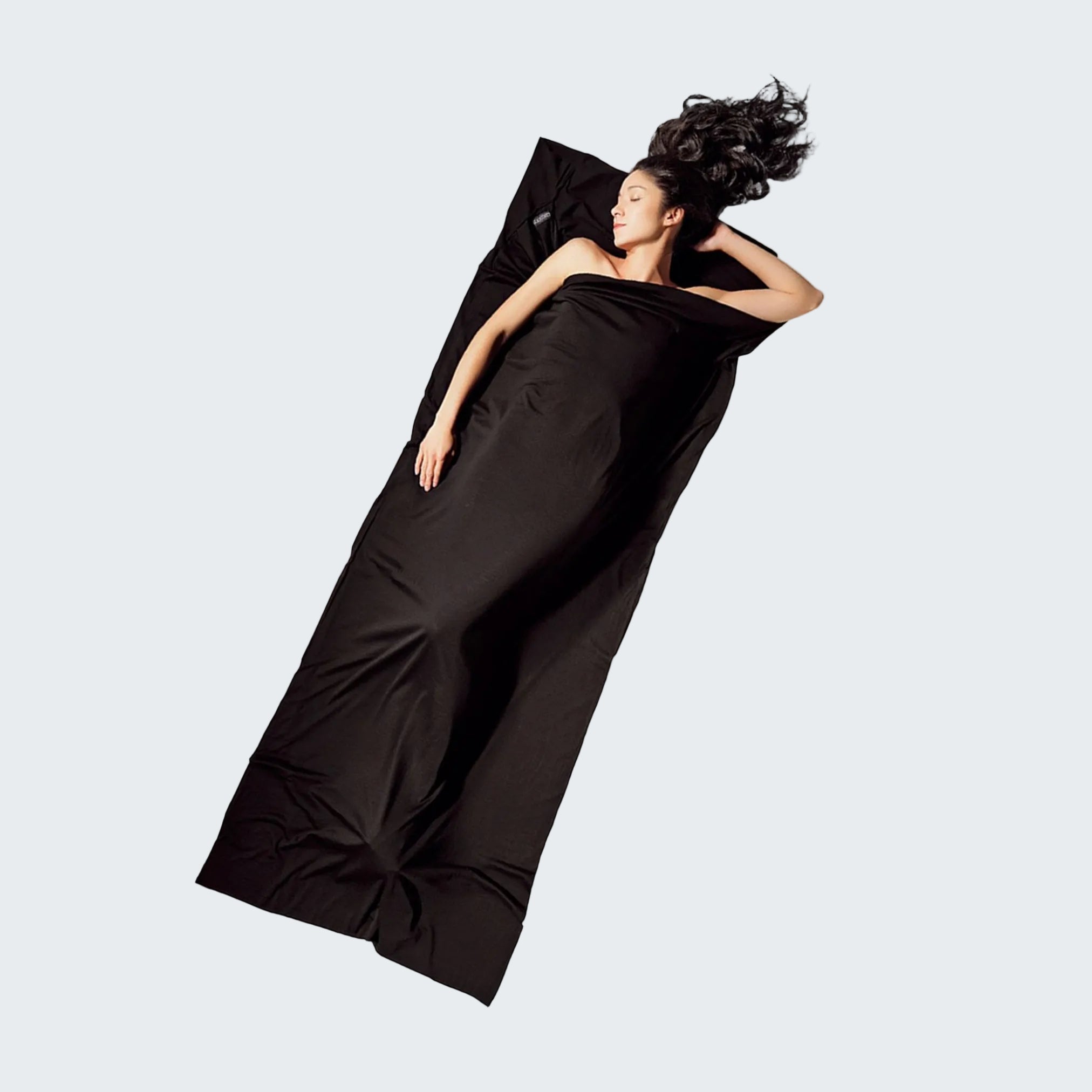 Woman lying on a black sleeping bag against a light gray background