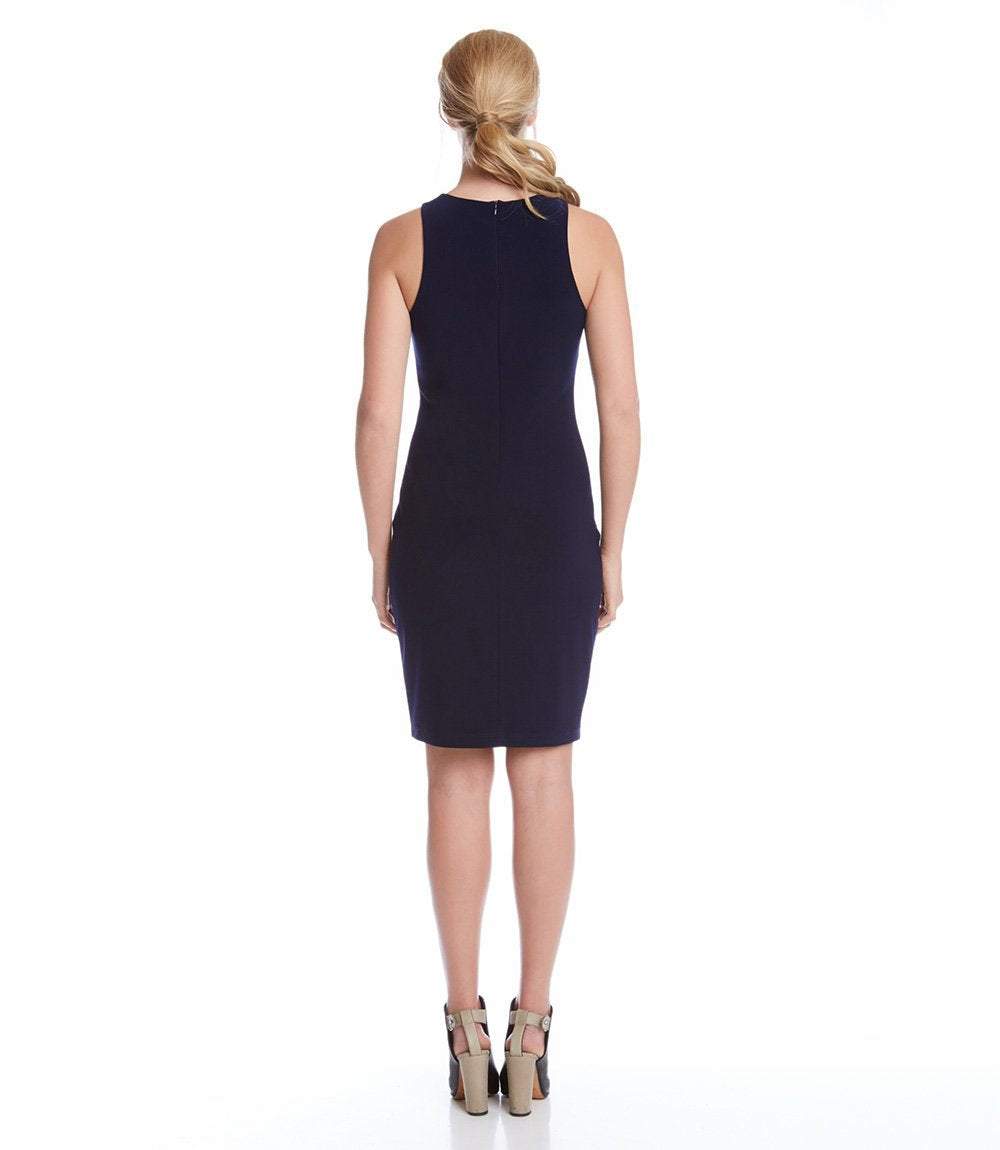 A woman viewed from the back wearing a sleeveless, knee-length navy dress and beige high-heeled sandals against a plain white studio background.